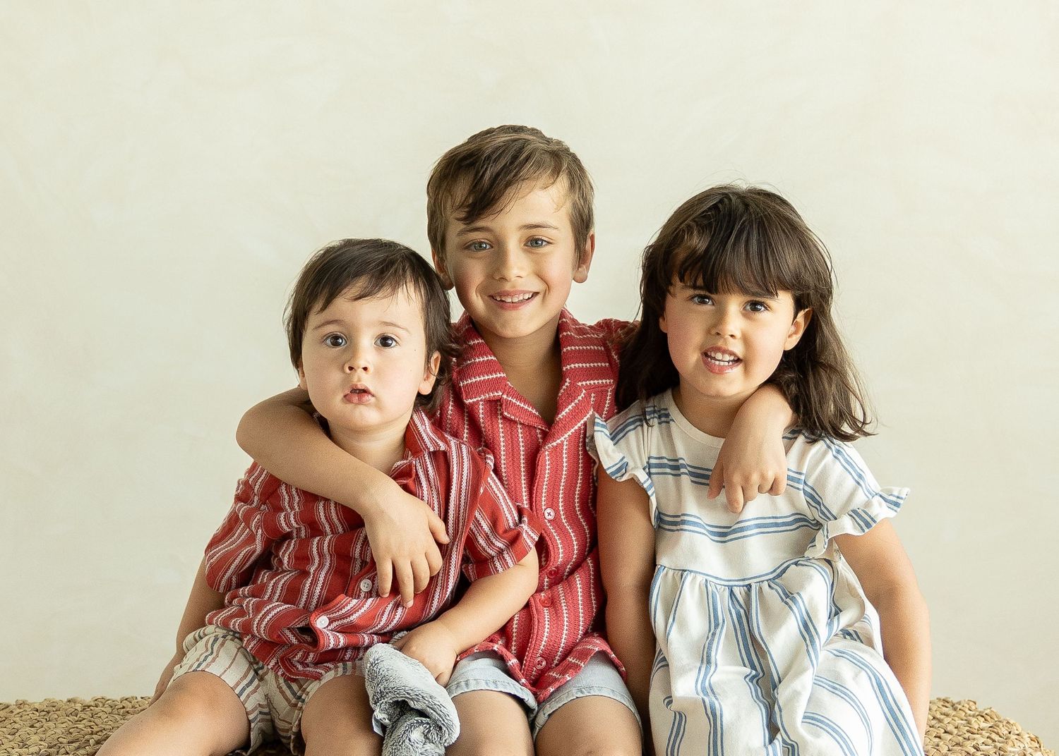 Three young siblings pose together smiling, wearing colorful striped outfits against a neutral background. Roanoke, VA