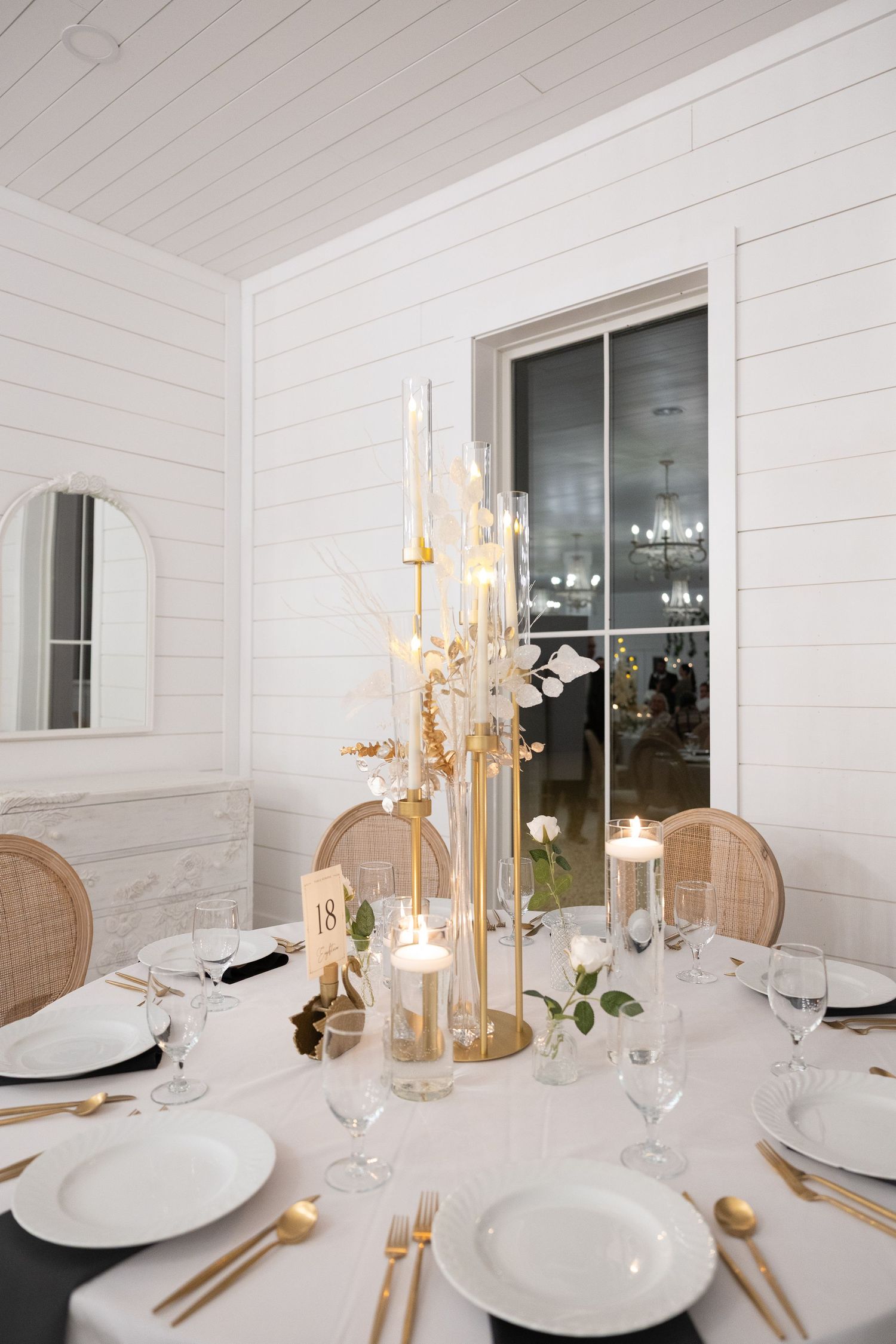 Elegant wedding reception table with gold candelabra centerpiece, white linens, gold cutlery, and glassware in a bright white venue.