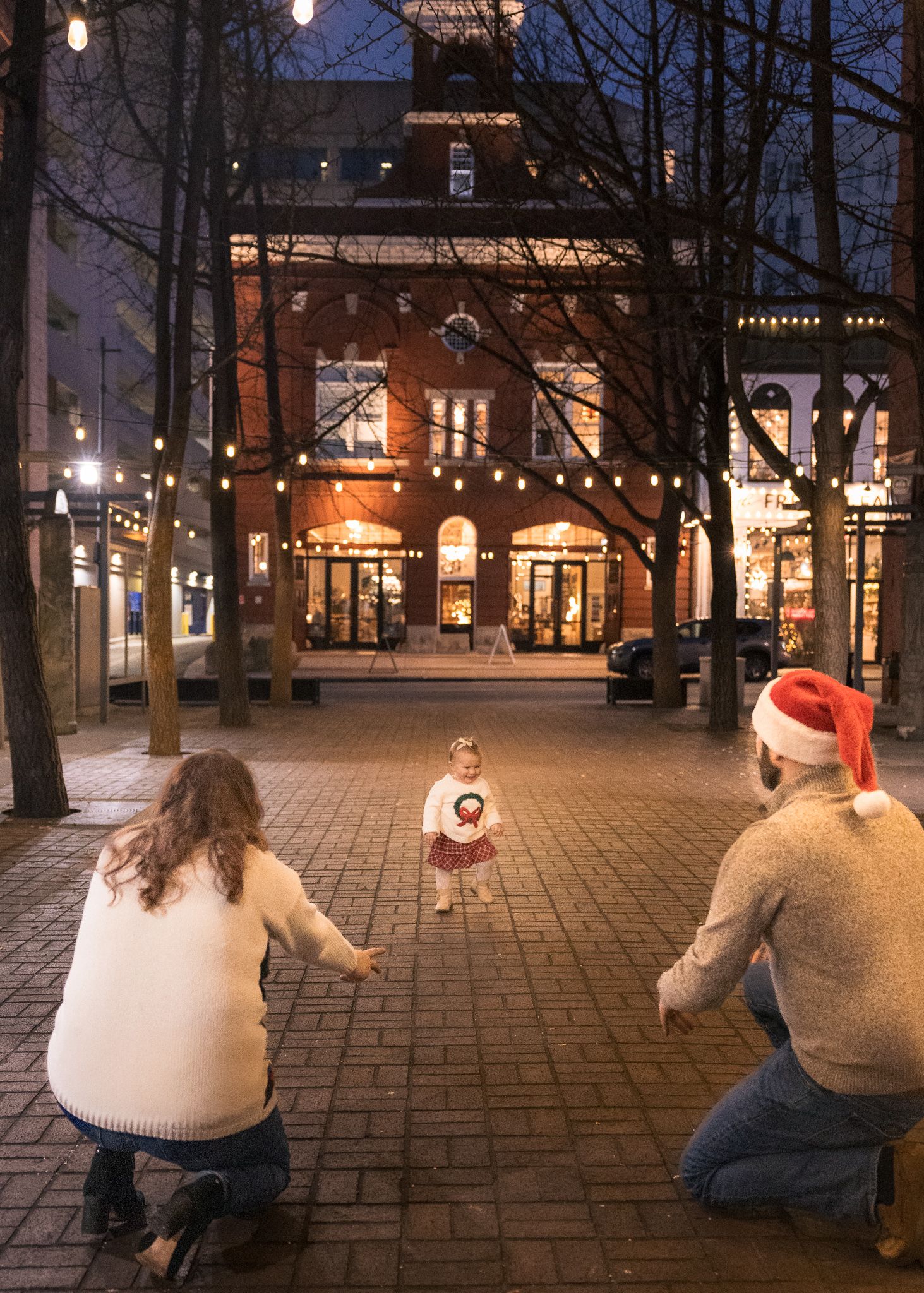 Family with toddler enjoying festive outdoor plaza decorated with string lights and brick buildings at Christmas. Downtown Roanoke, VA