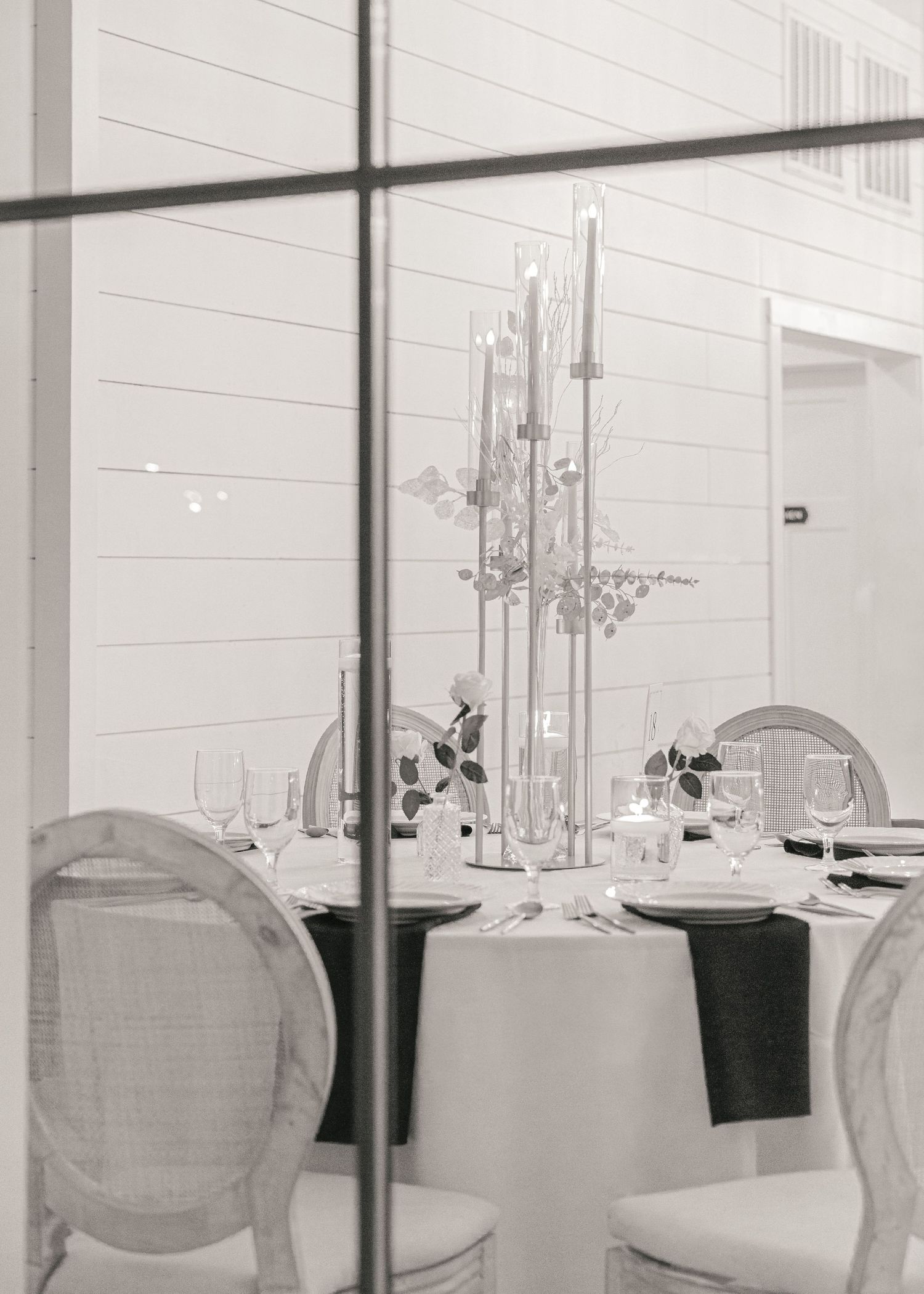 Elegant black and white dining table setup with tall candelabra centerpiece, glassware, and French chairs in a bright venue.