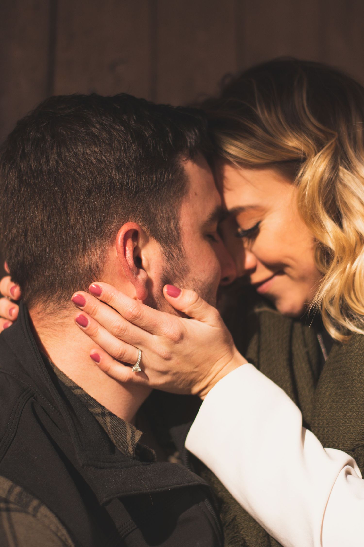 A couple shares a romantic moment, woman with red nails and ring gently cups man's face as they lean in close.