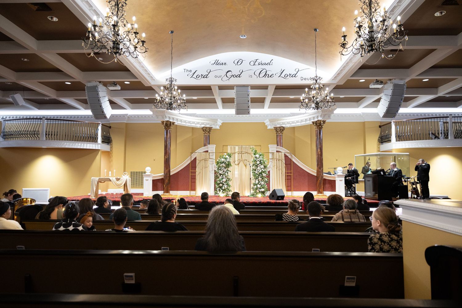 Elegant church wedding ceremony with wooden pews, floral altar, chandeliers, and scripture inscription above the stage.