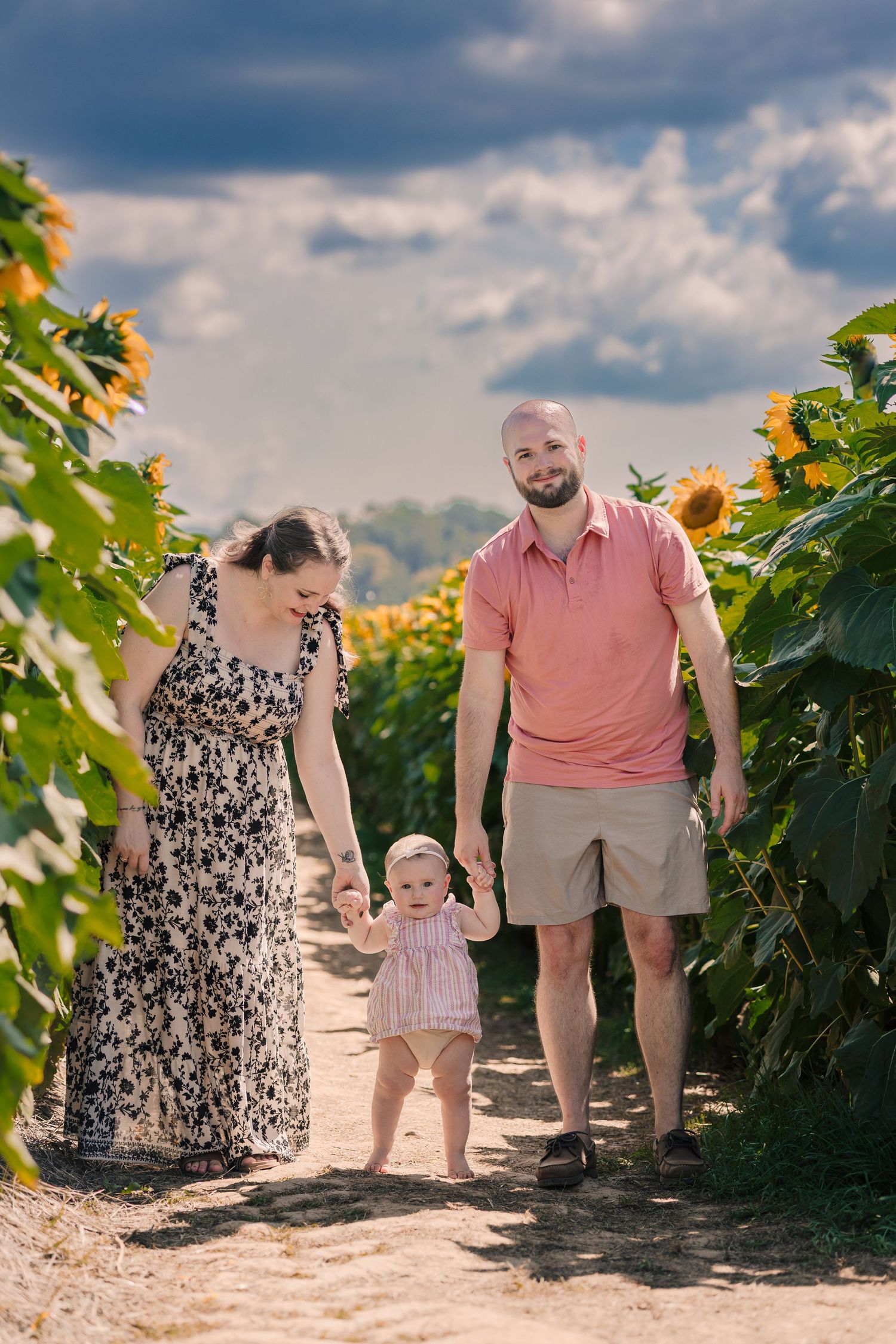 Family with baby walking through sunflower field on sunny day.