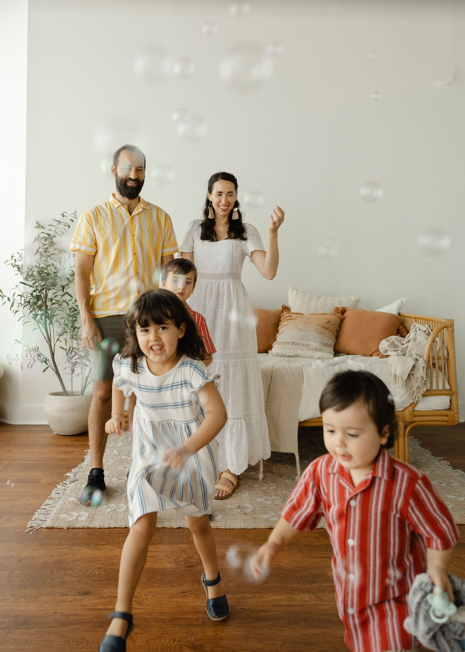 A joyful family of five plays with bubbles indoors, children laughing and running in a bright, cozy living room.