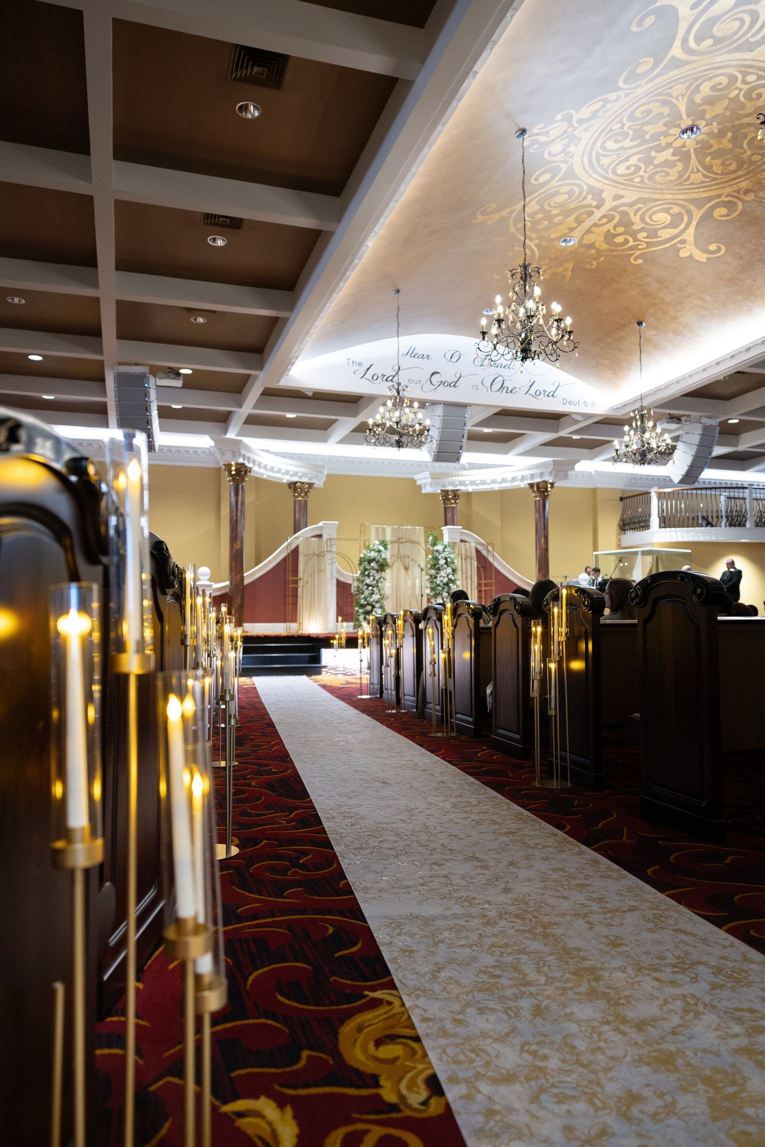 Elegant wedding chapel aisle with white runner, candle stands, dark wood pews, and floral altar decorations.