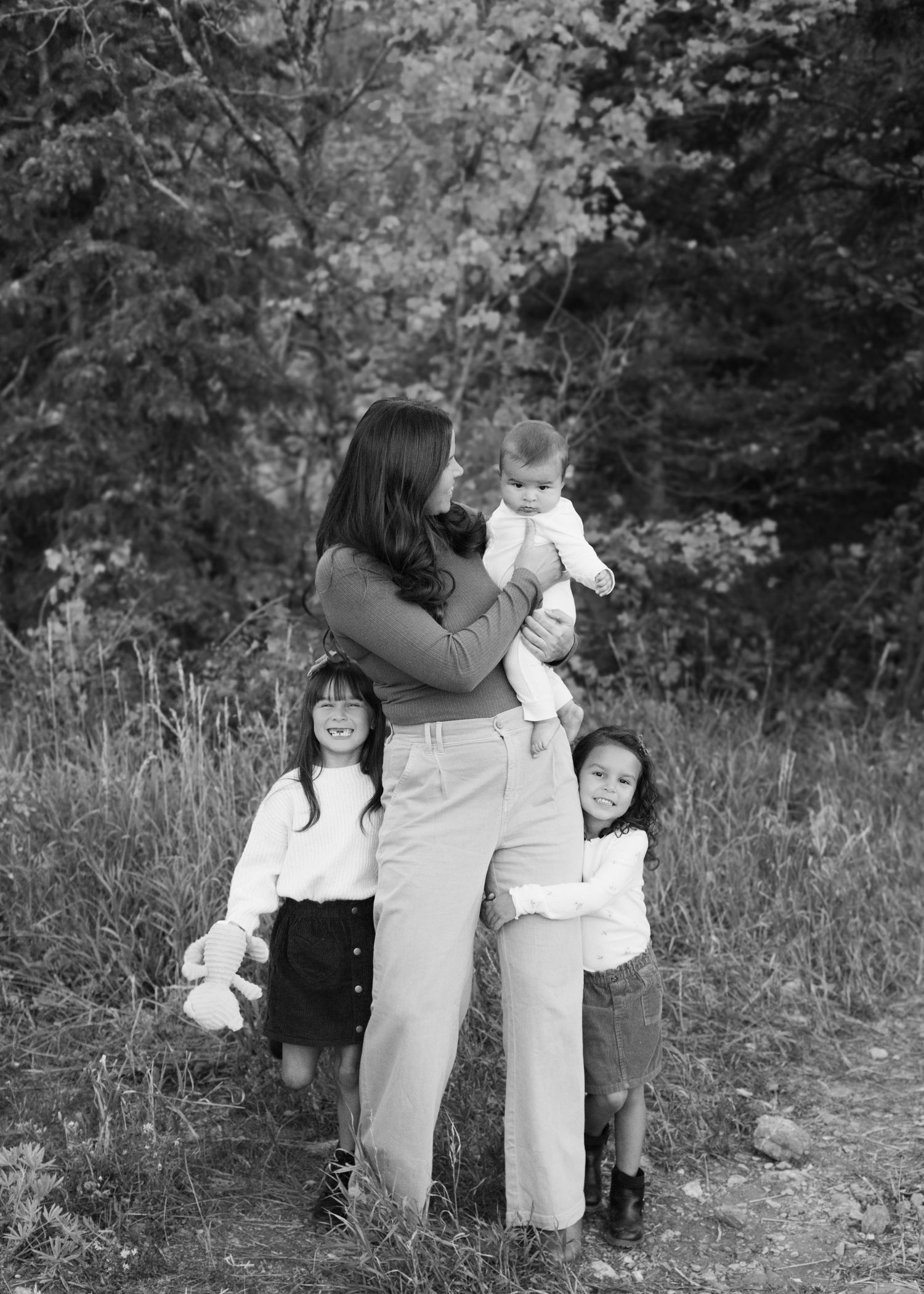 Black and white photo of a mother holding a baby while two young girls stand beside her outdoors.