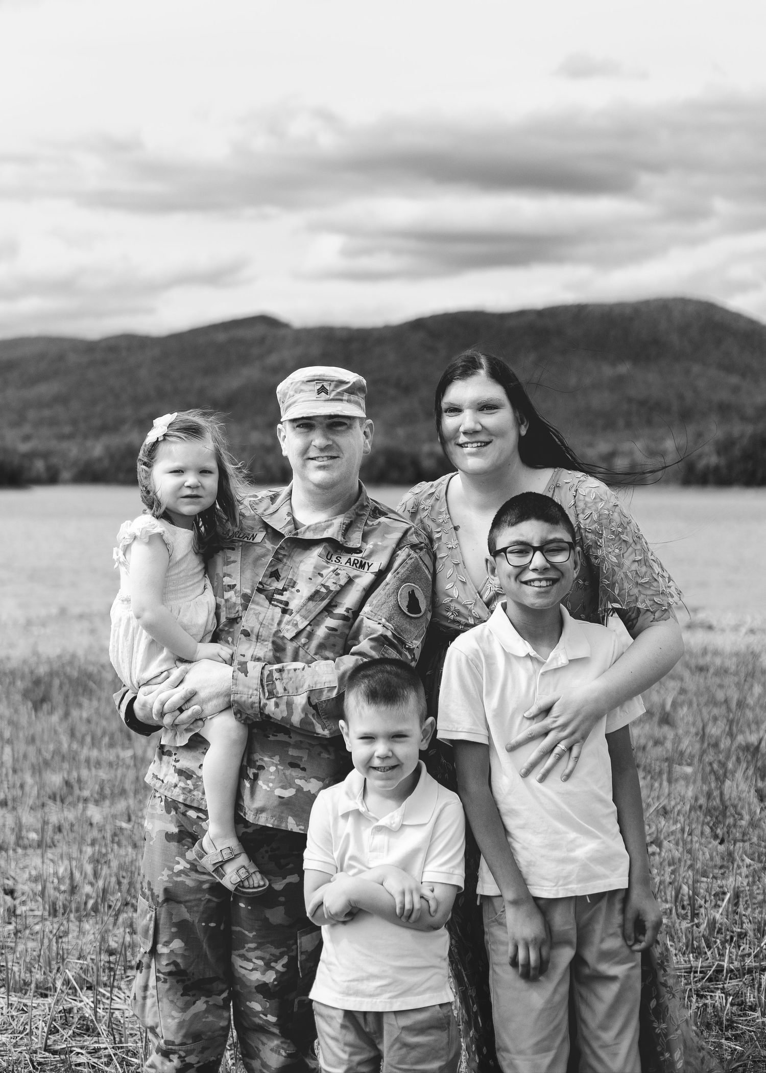 Black and white family portrait of a soldier in uniform with wife and three children in a scenic field.