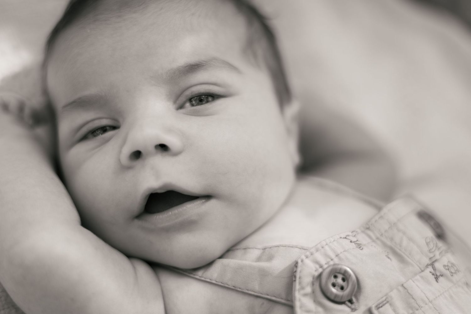 Close-up black and white portrait of a newborn baby smiling, cradled in an adult's hands.