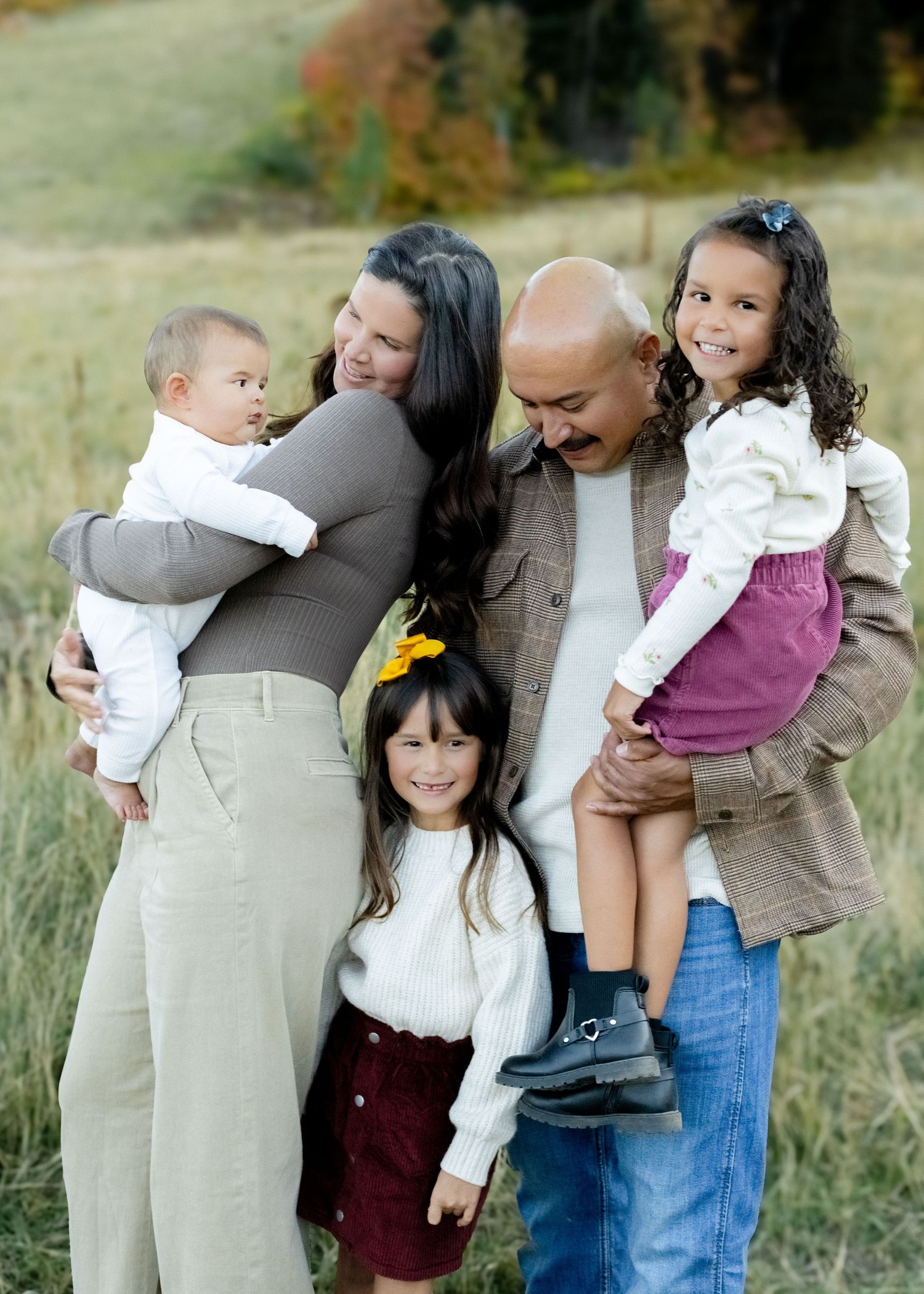 A happy family of five poses outdoors in a field, with parents holding three young children during a fall photo session.