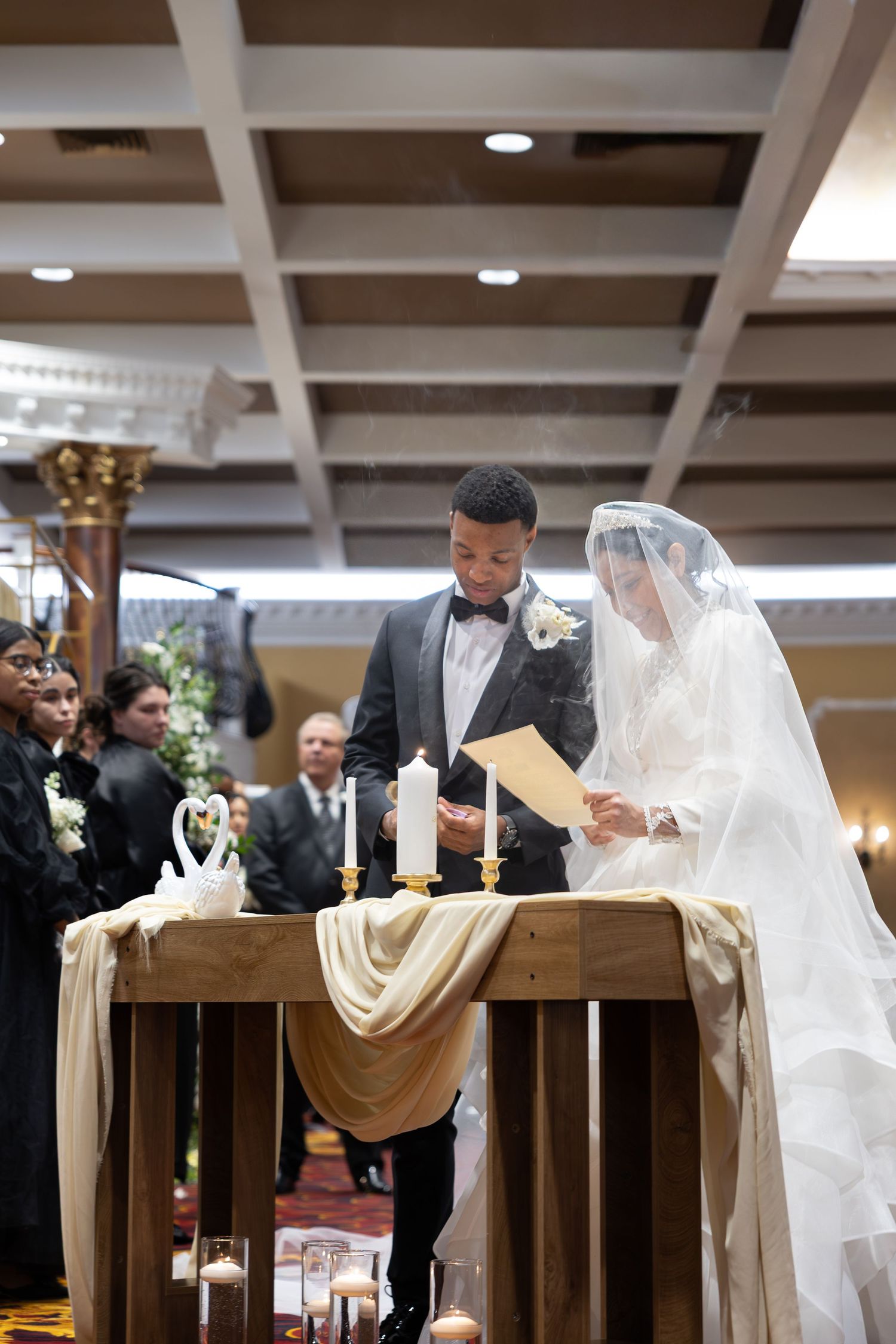 Bride and groom exchanging vows at wedding altar with candles and white swan decorations.