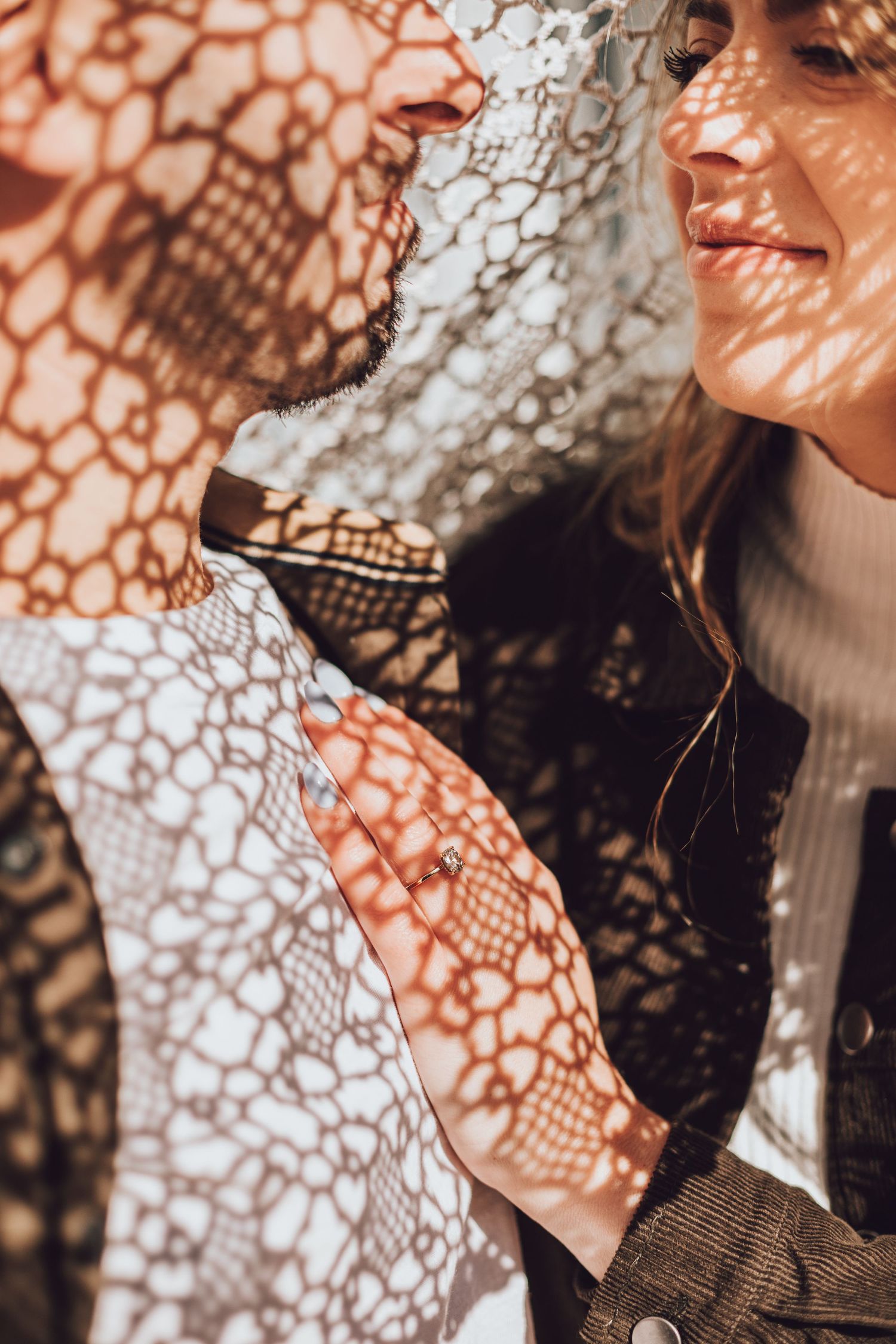 Couple bathed in dappled sunlight through lace, creating intricate shadow patterns on their faces and clothing.