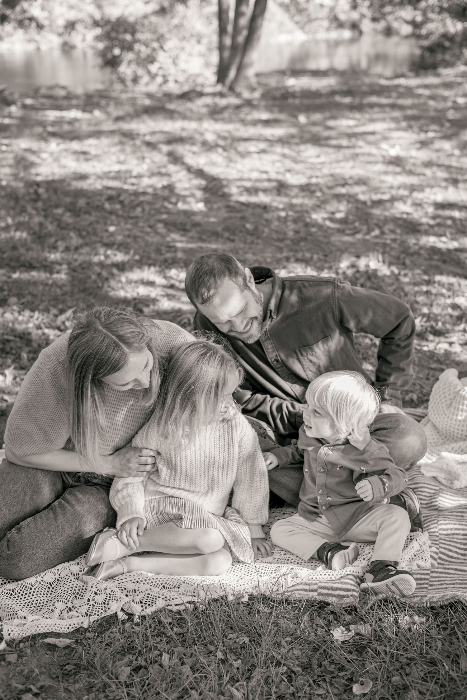 Black and white family photo of parents with two young children sitting on a blanket in a park.