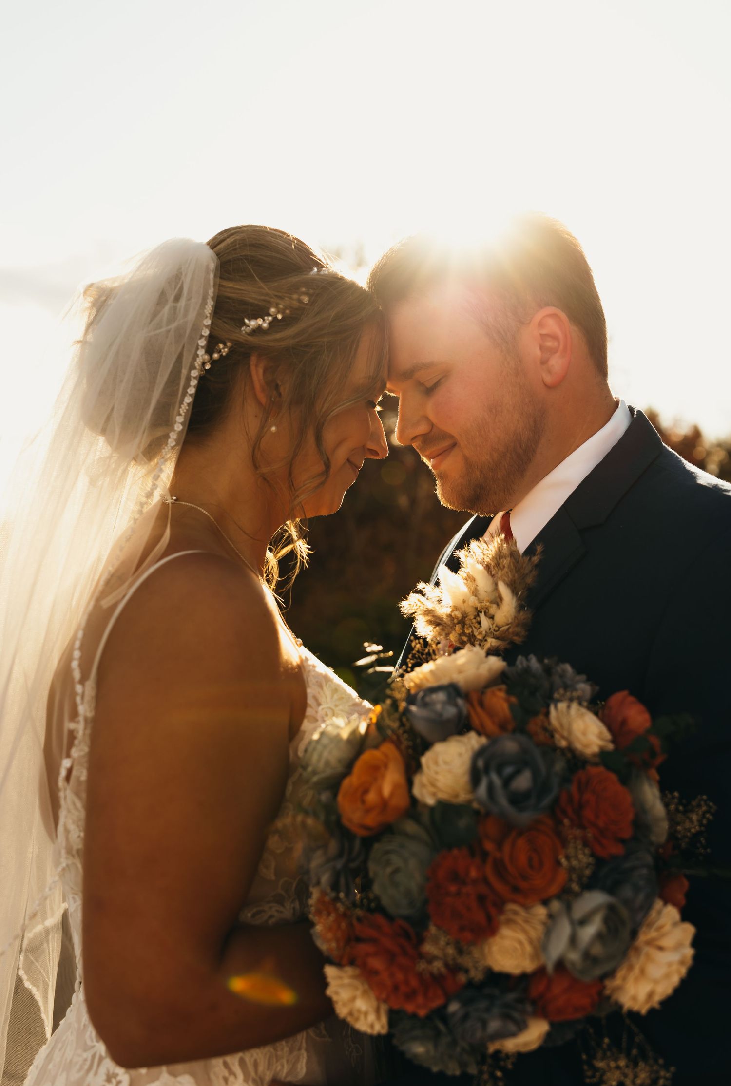 Intimate backlit wedding portrait with autumn-colored floral bouquet.