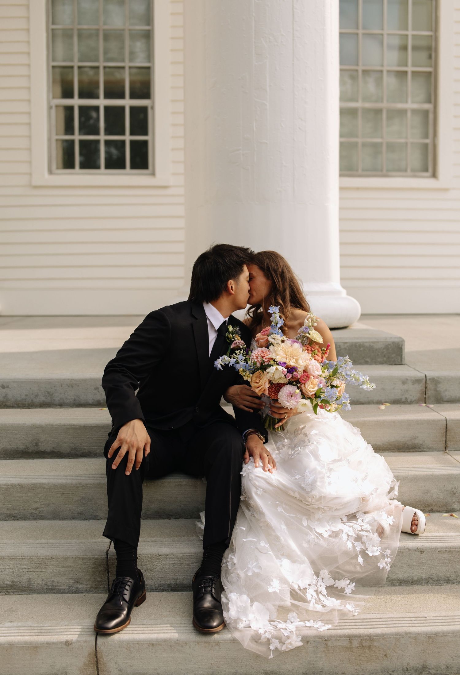 Tender wedding moment shared on white church steps with floral bouquet.