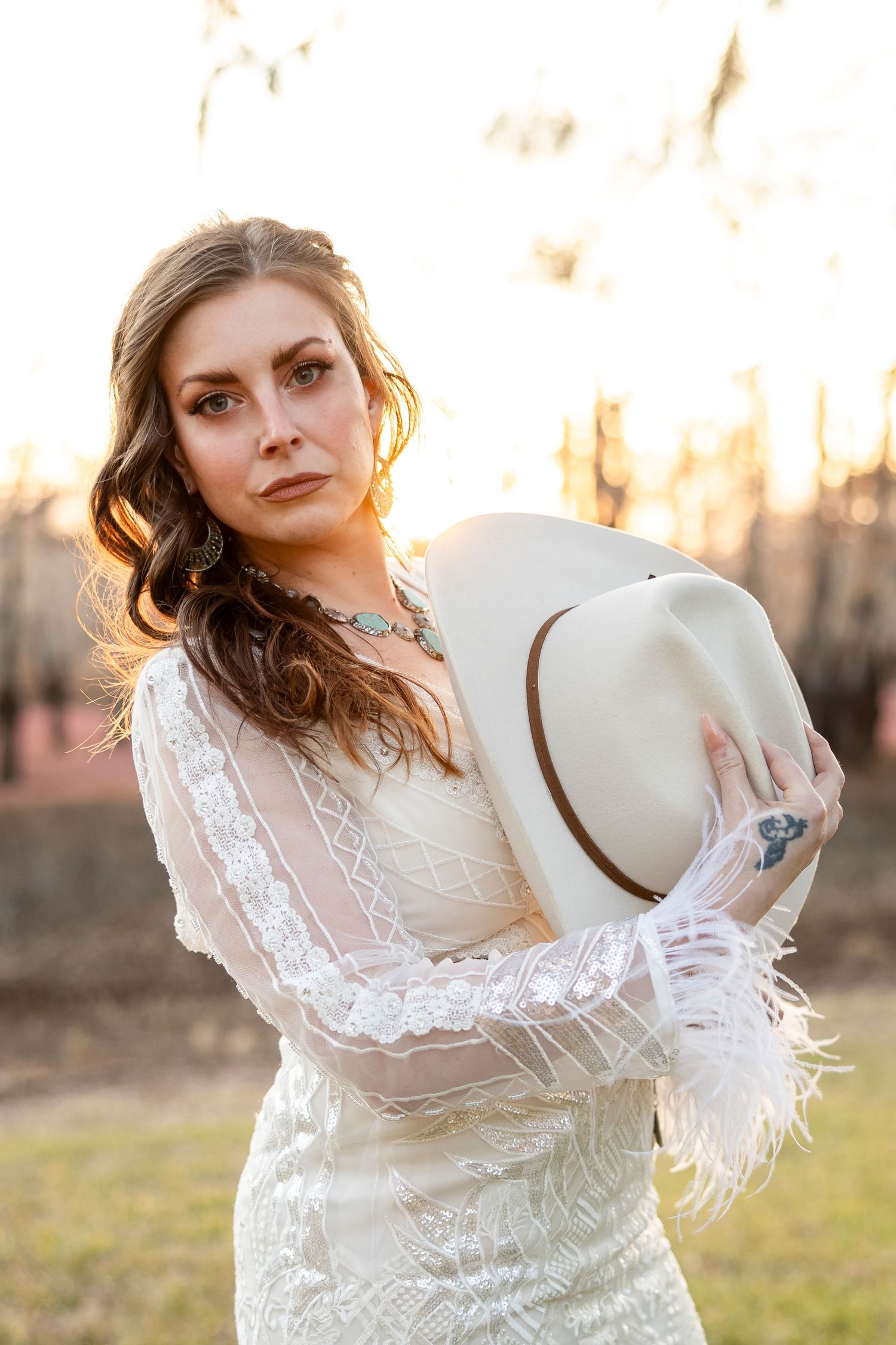 Woman in vintage-inspired white lace dress poses outdoors at sunset creating romantic bridal portraits.