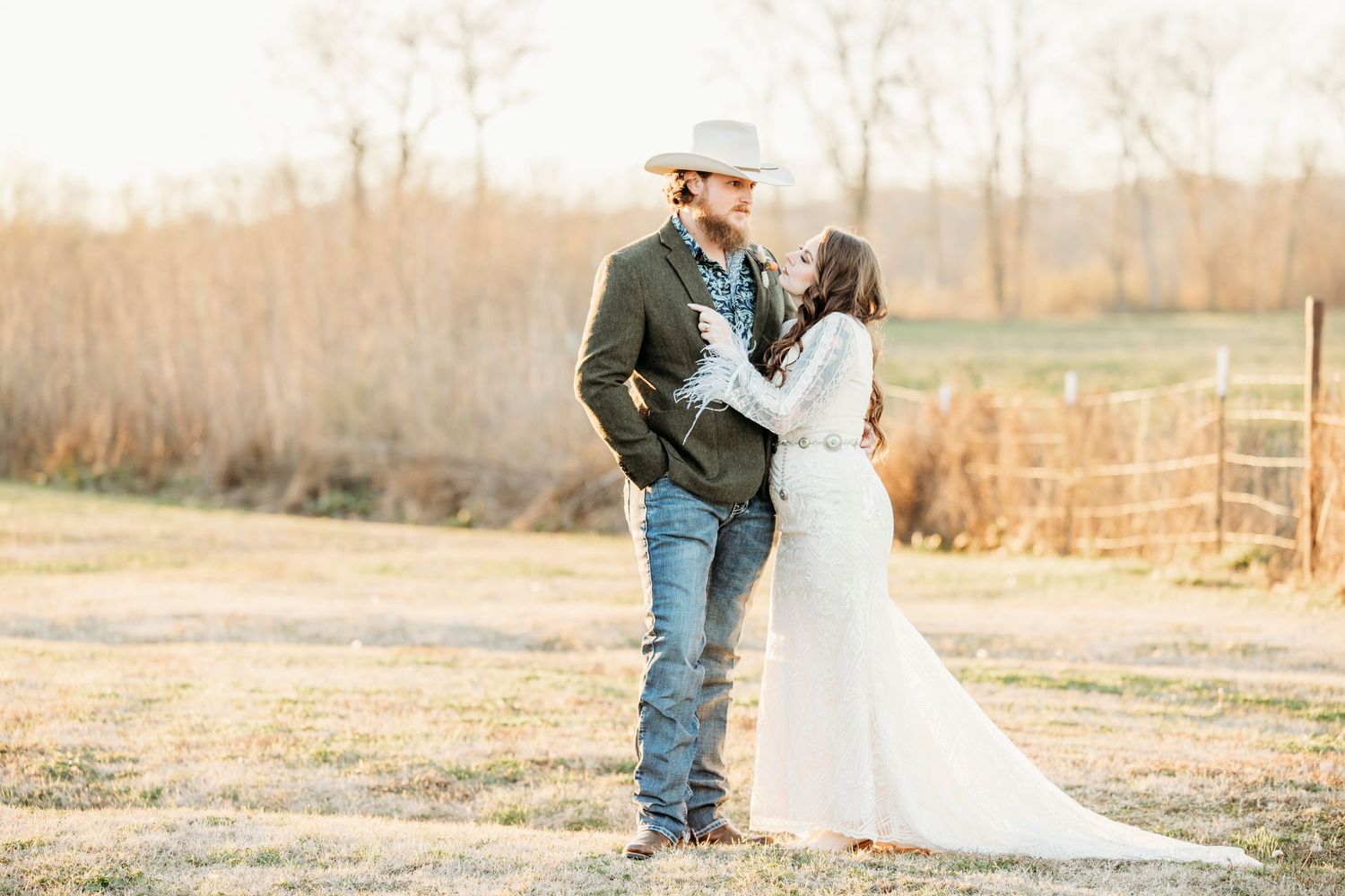 A couple embraces in a romantic outdoor setting during golden hour in a rustic field.