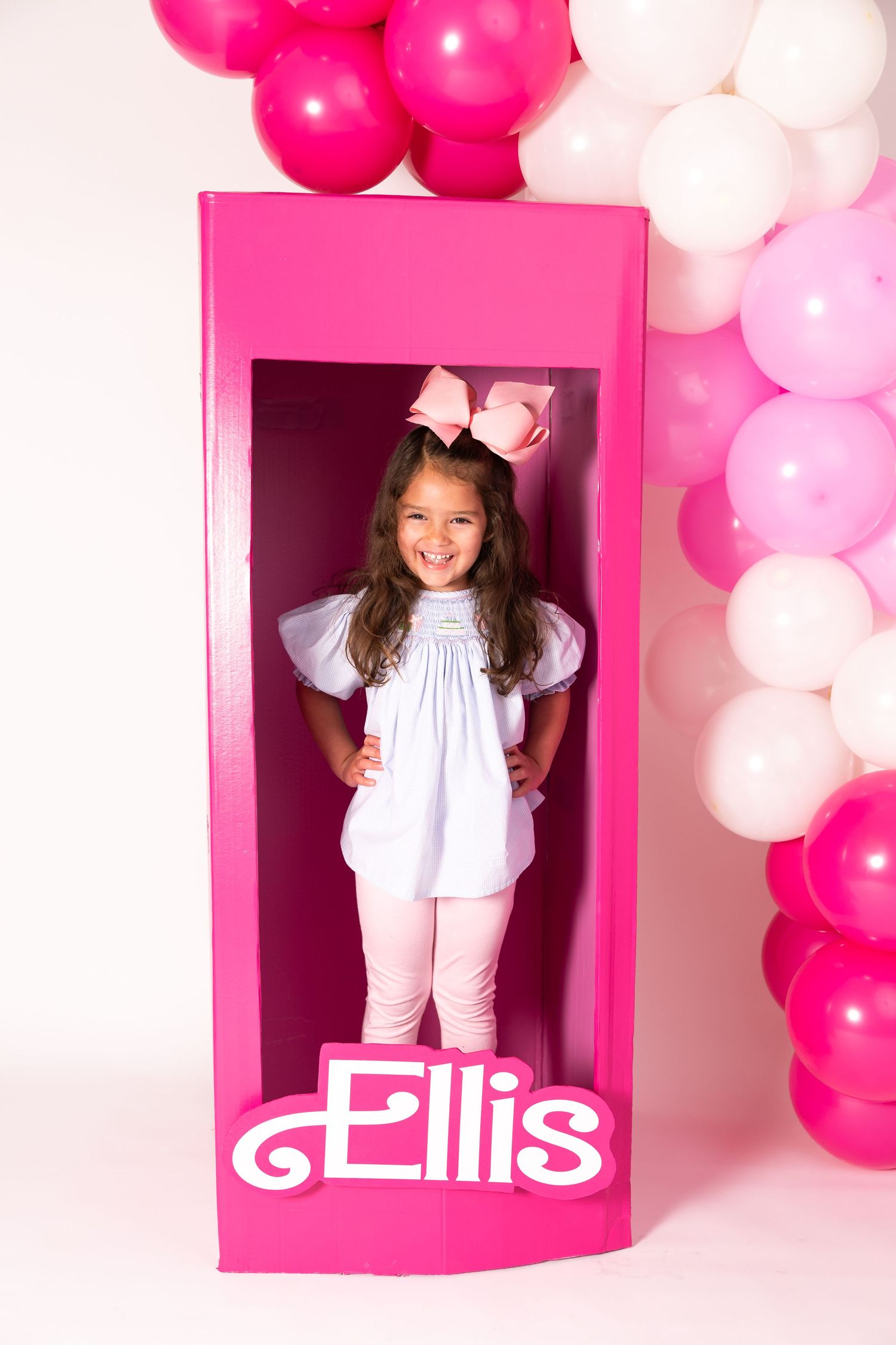 Life-sized pink Barbie-style doll box display with balloons decorated with pink and white balloon arch.