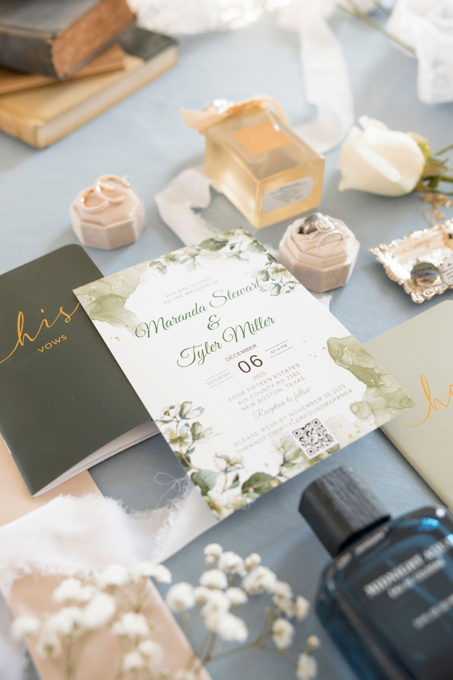Elegant wedding invitation for Miranda Stevens and Tyler Miller displayed with floral decor, ring boxes, and perfume bottles.