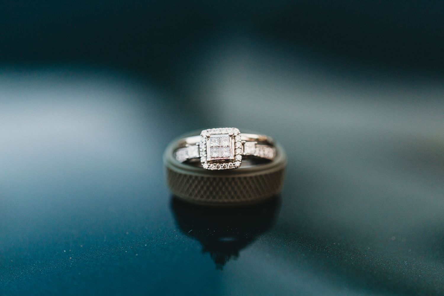 A silver diamond engagement ring sparkles against a dark reflective surface in dramatic lighting.
