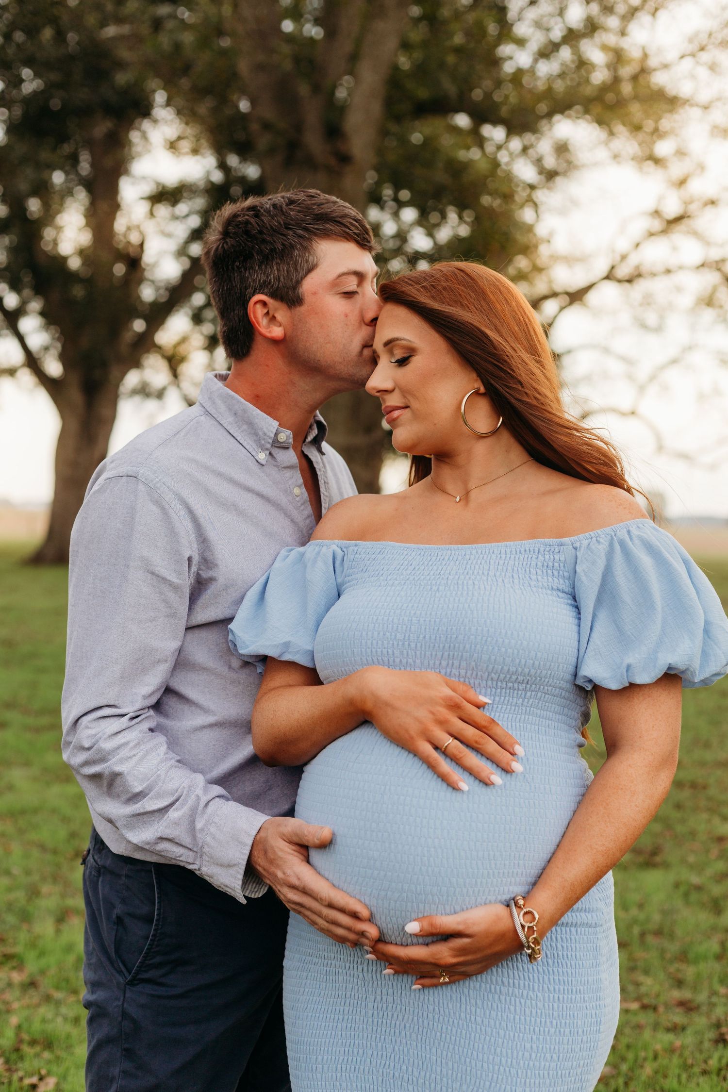 A loving maternity photo of a couple outdoors at sunset with the expectant mother wearing a light blue off-shoulder dress.