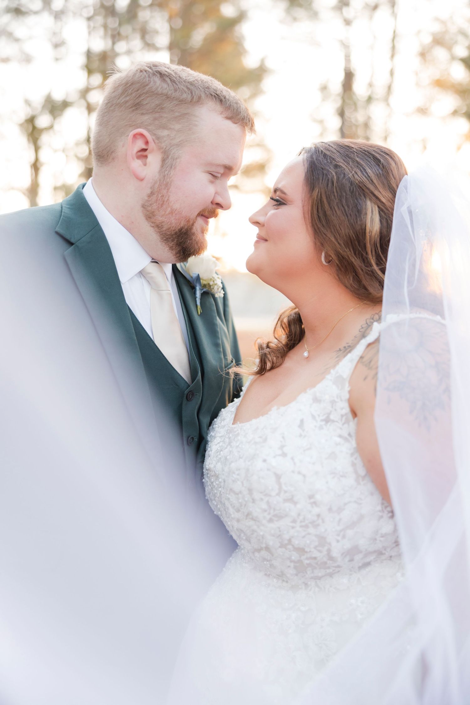 A bride and groom share a romantic moment gazing at each other, framed by a flowing veil in soft golden light.