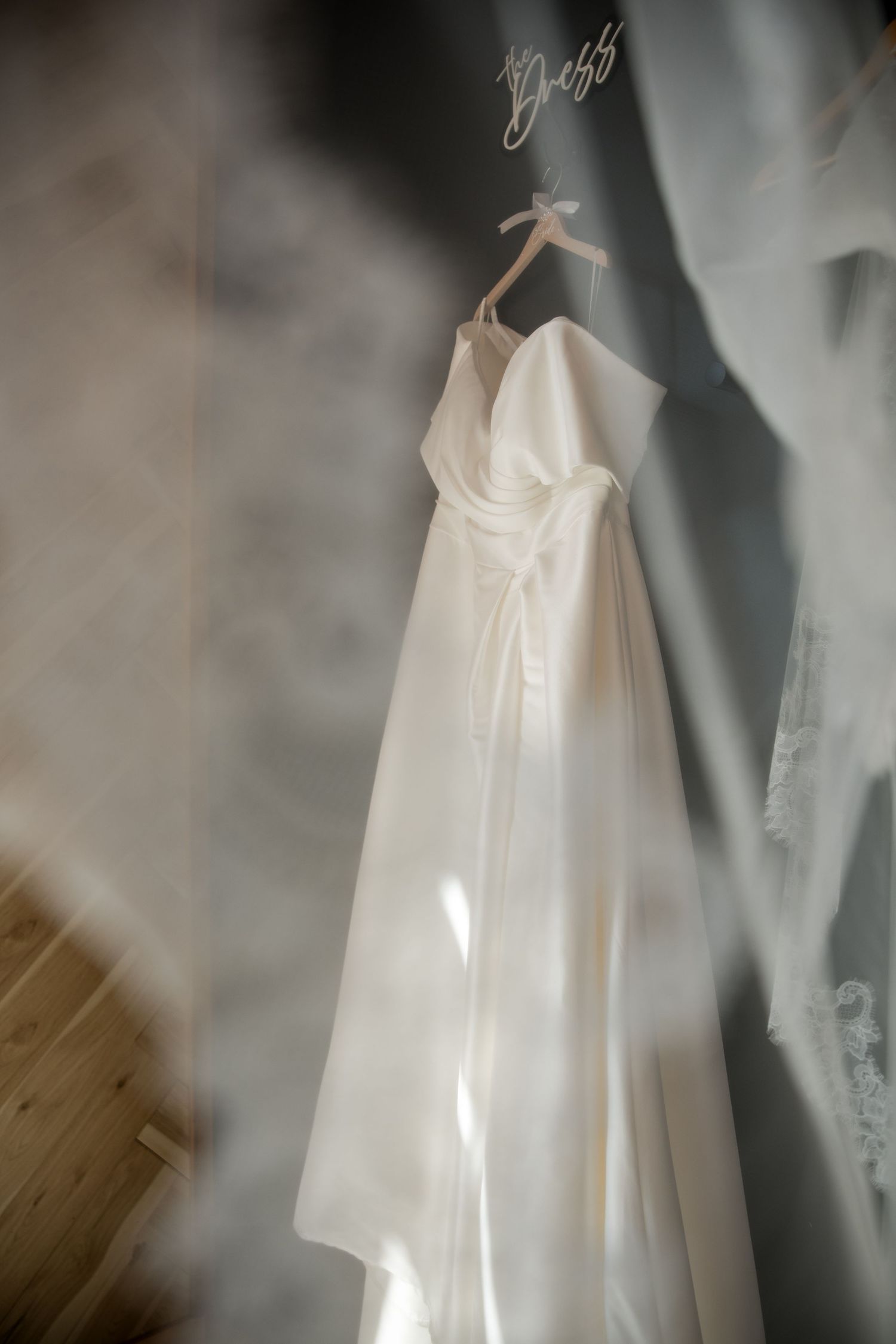 Elegant white wedding dress hanging on a decorative hanger, bathed in soft natural light against a neutral wall.