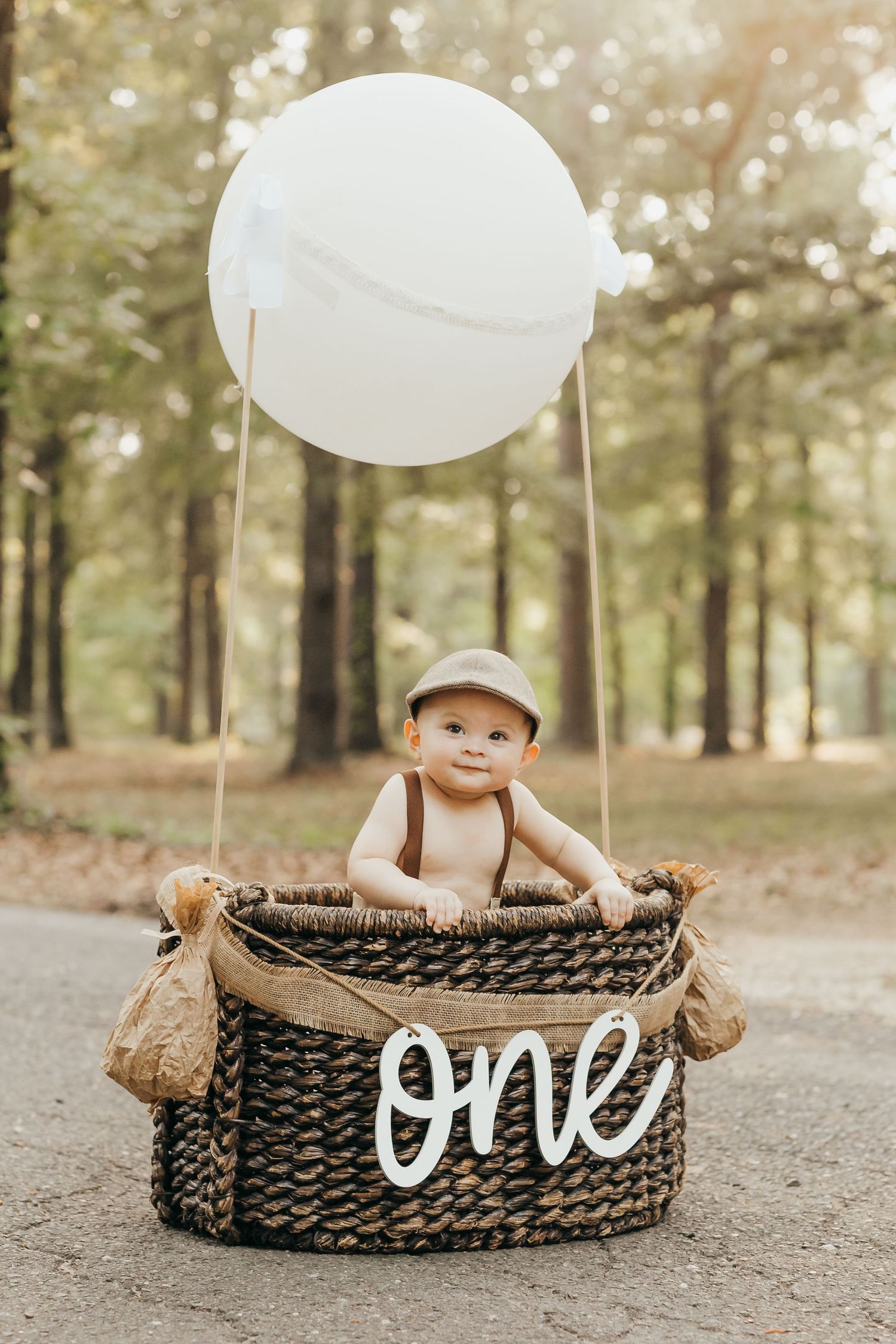 First birthday photo shoot in forest featuring woven basket decorated with 'one' text and large white balloon.