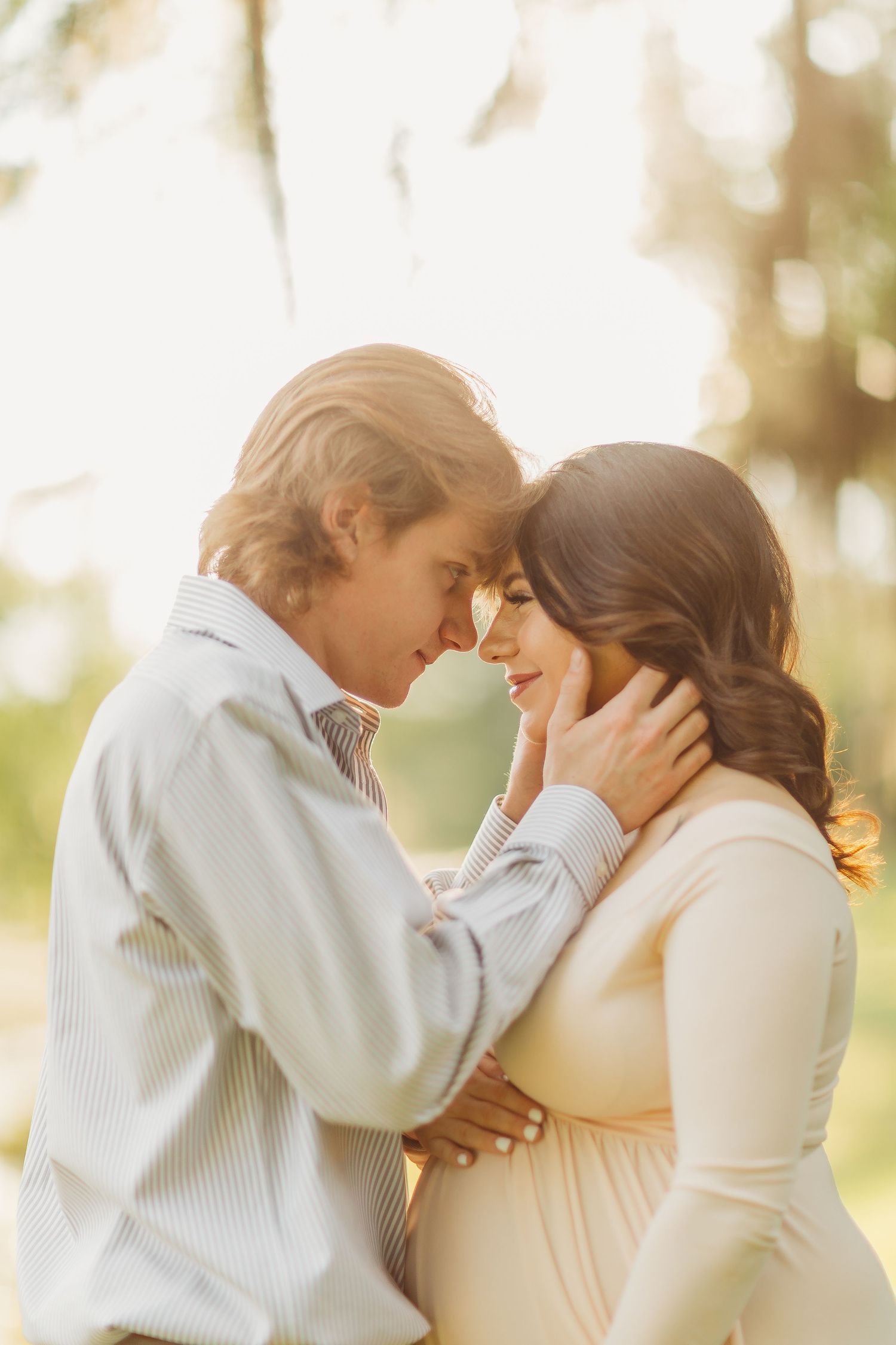 A tender romantic moment between a couple embracing in soft golden sunlight outdoors.