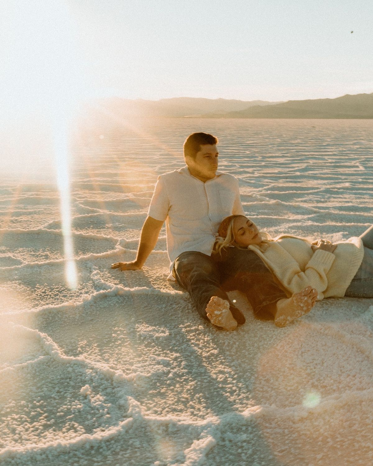 A person lies down on the salt flats at sunset, creating a dreamy ethereal scene in warm golden light.