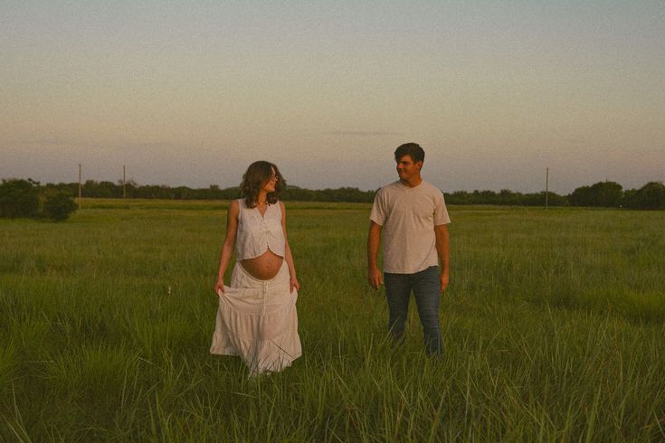 A couple walks through a serene green meadow at sunset, holding hands in the warm summer light.
