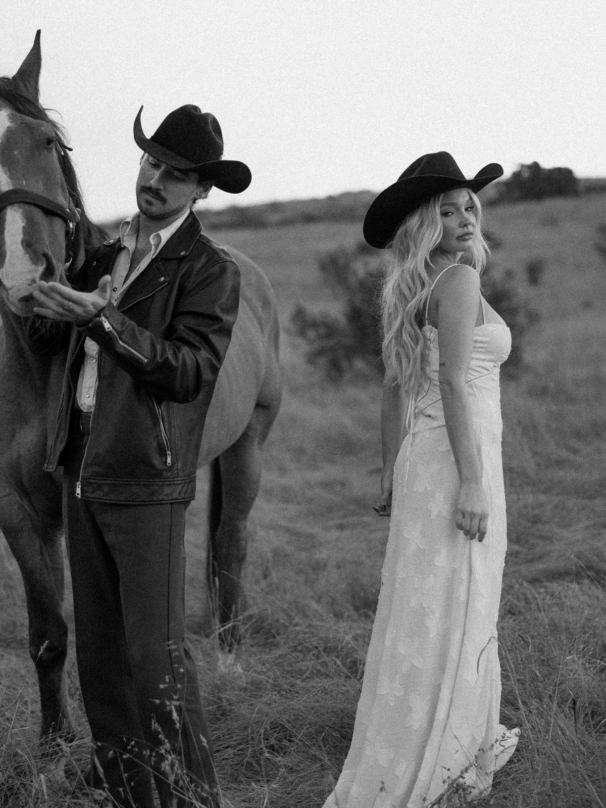 A black and white western-themed photo showing a cowboy with a horse and a woman in a flowing white dress in a field.