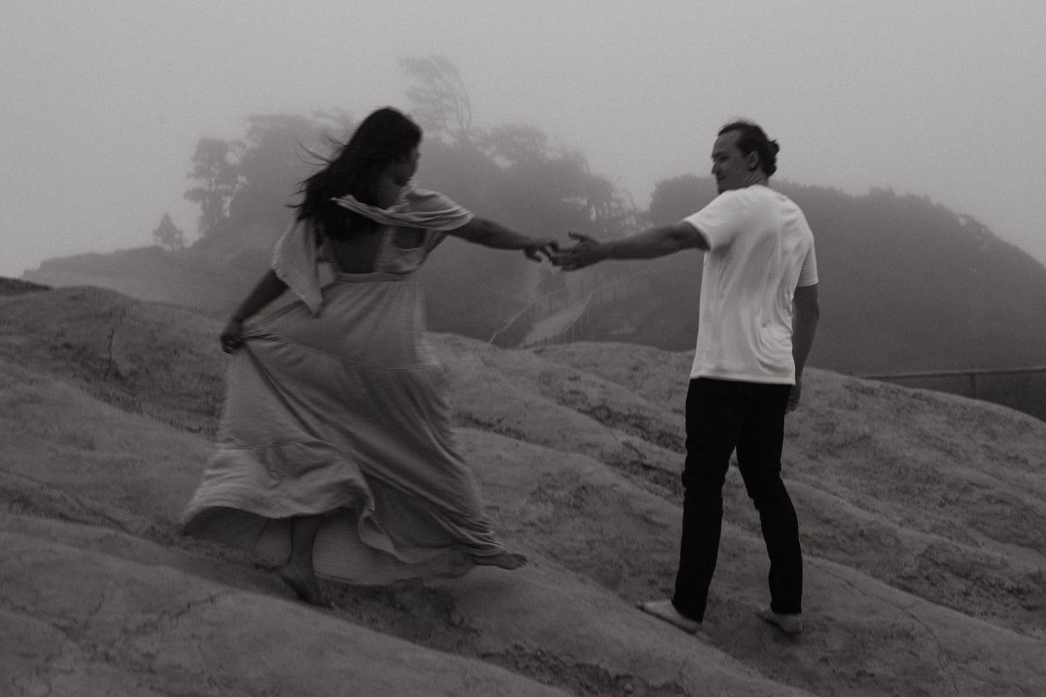 A couple dances on rocky terrain in a misty, foggy landscape in a black and white photo.