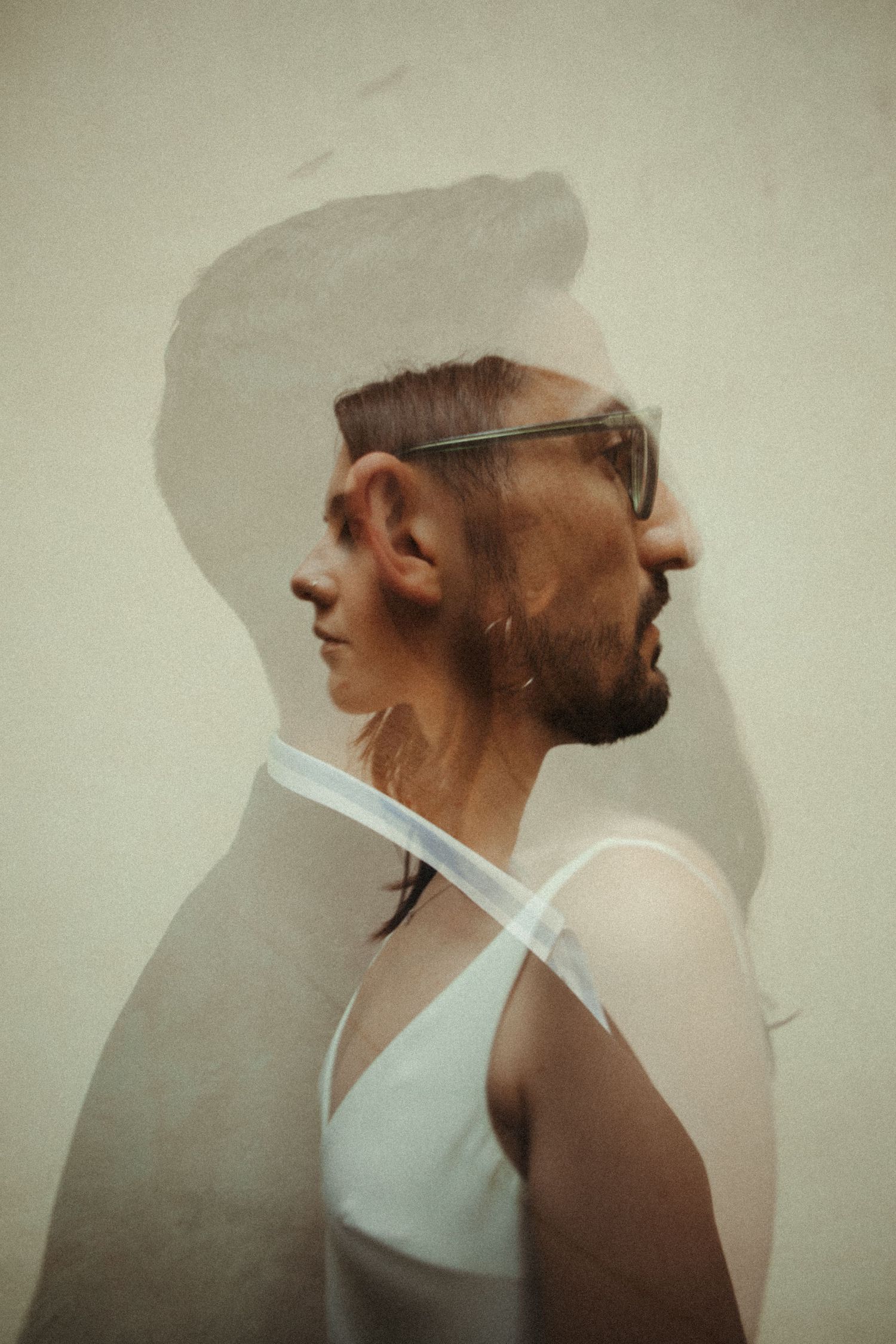Double exposure portrait of a woman and bearded man with glasses, creating a surreal layered effect.