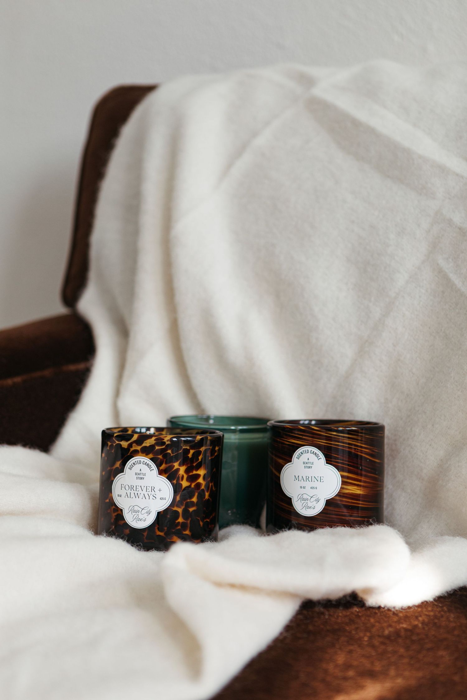 Small glass jars with decorative labels sit nestled in white fabric, creating a cozy product photography scene.
