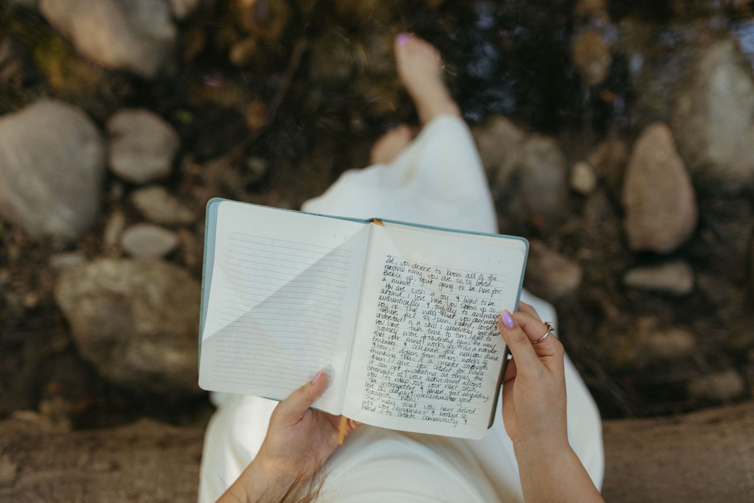 Hands holding open pages of a book against a rocky natural background.
