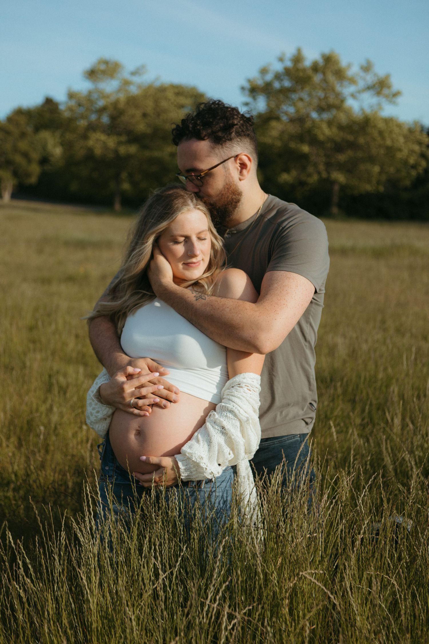 A couple embraces tenderly in a golden field during sunset, celebrating pregnancy.