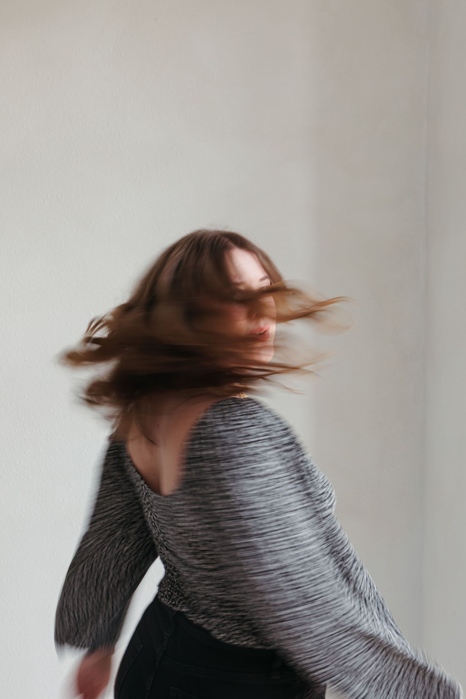 A person with brown hair wearing a striped gray sweater spins around in a dynamic motion blur sequence.