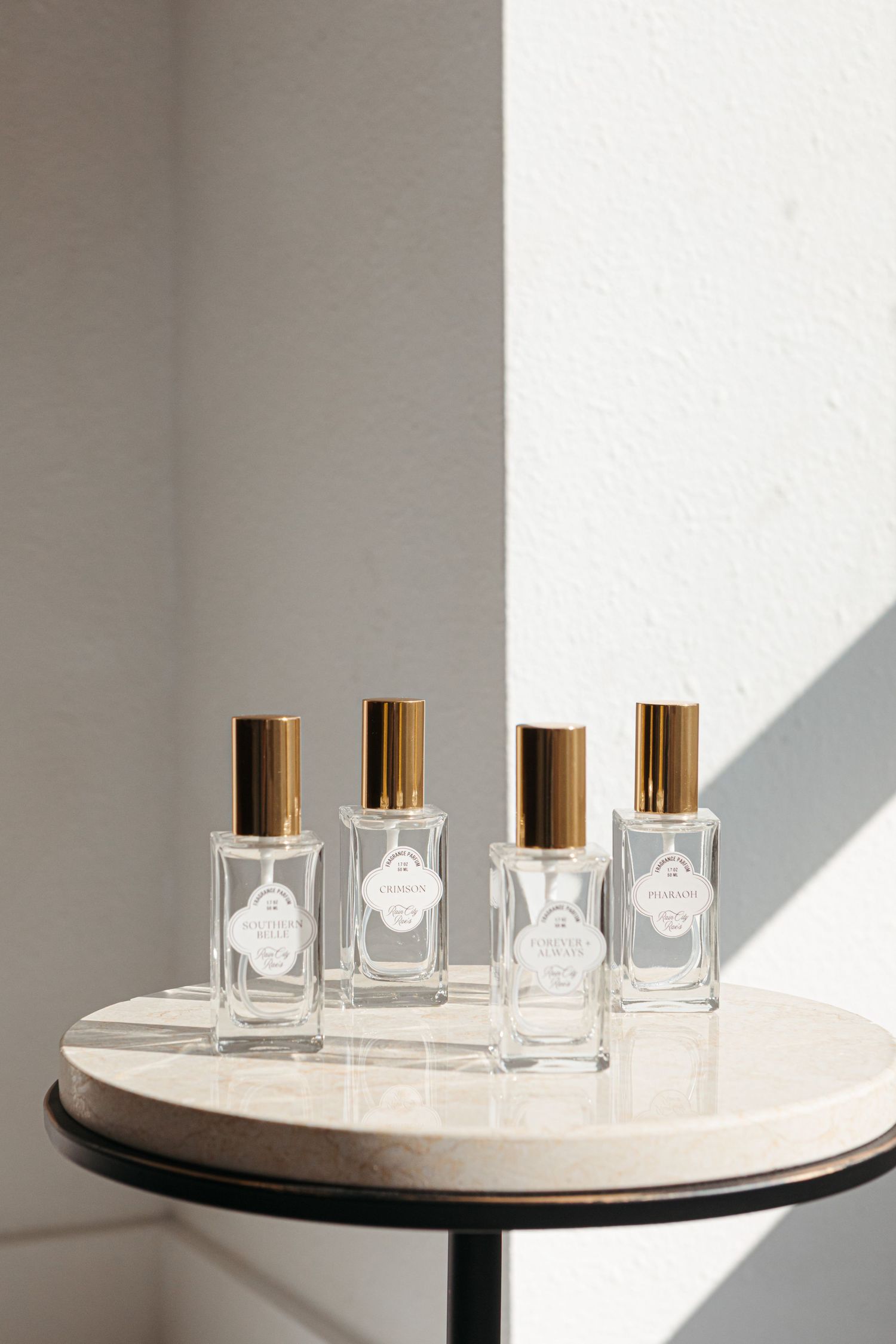 Four elegant glass perfume bottles with gold caps arranged on a white marble table casting dramatic shadows.