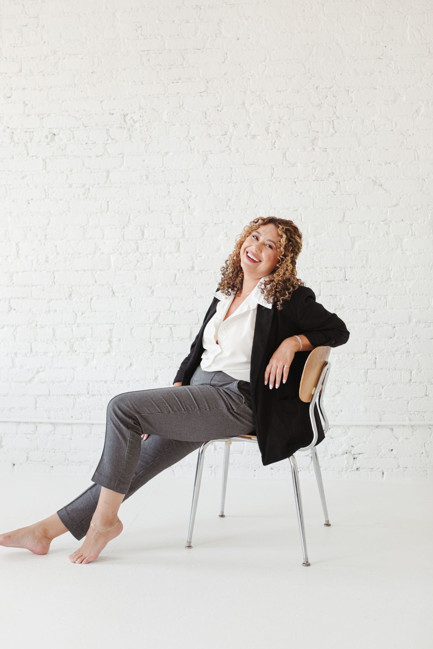 A figure in black and grey lounges gracefully across white chairs in a minimalist studio setting.