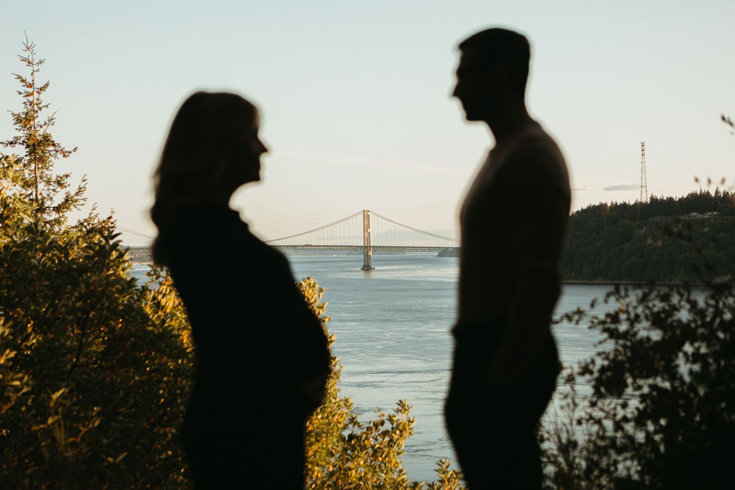 Six silhouetted figures stand along a coastal path with the Golden Gate Bridge visible in the distance at sunset.