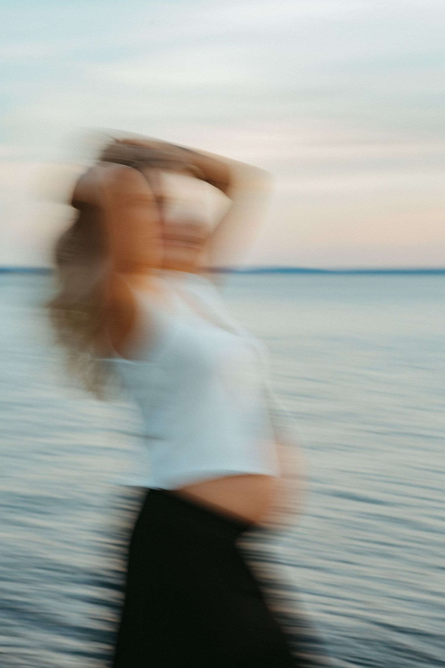 Motion blurred figure in white top and dark bottoms stands against serene ocean backdrop at dusk.