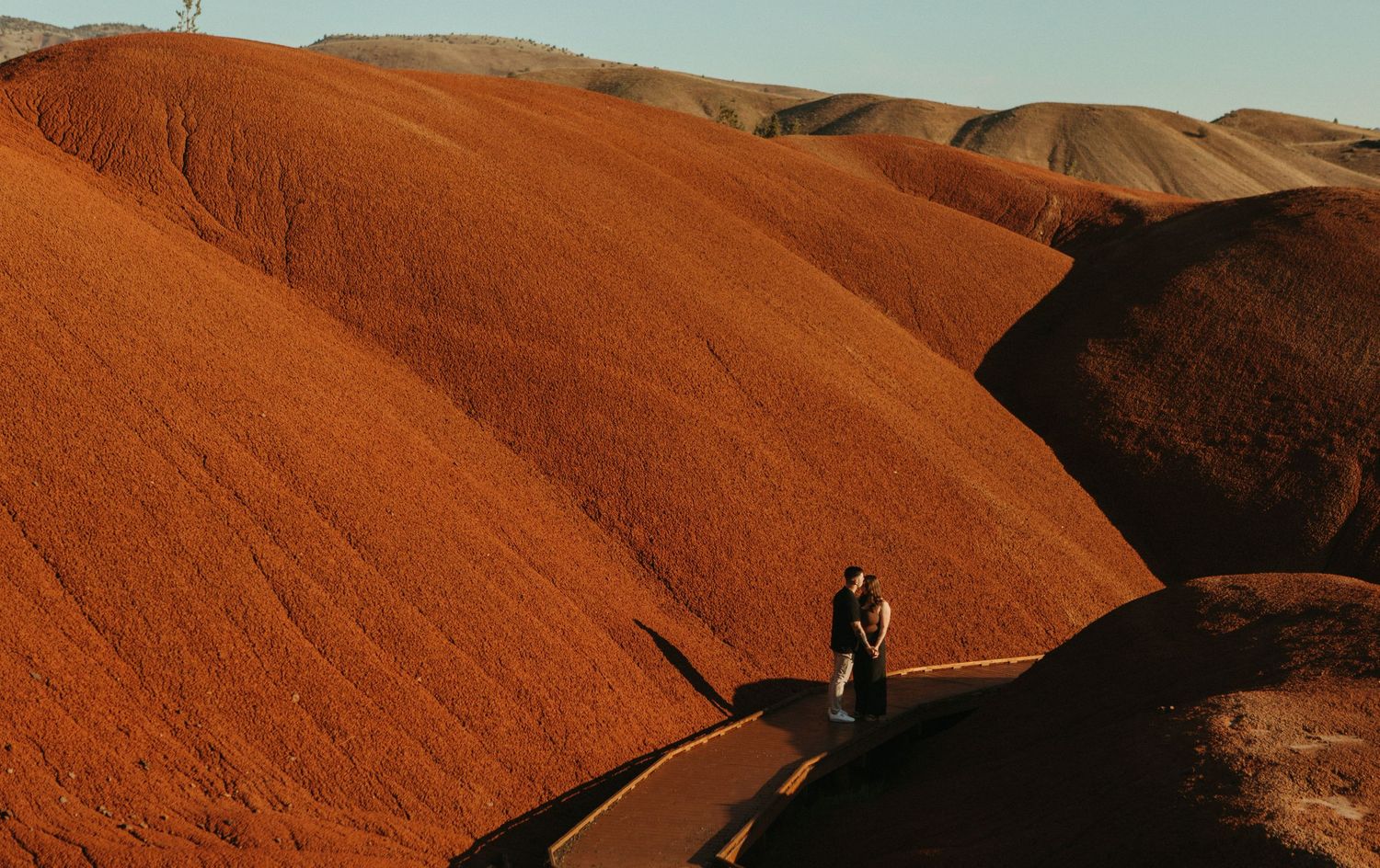 Couple embracing on a path surrounded by vivid red-orange hills at the Painted Hills, Oregon.