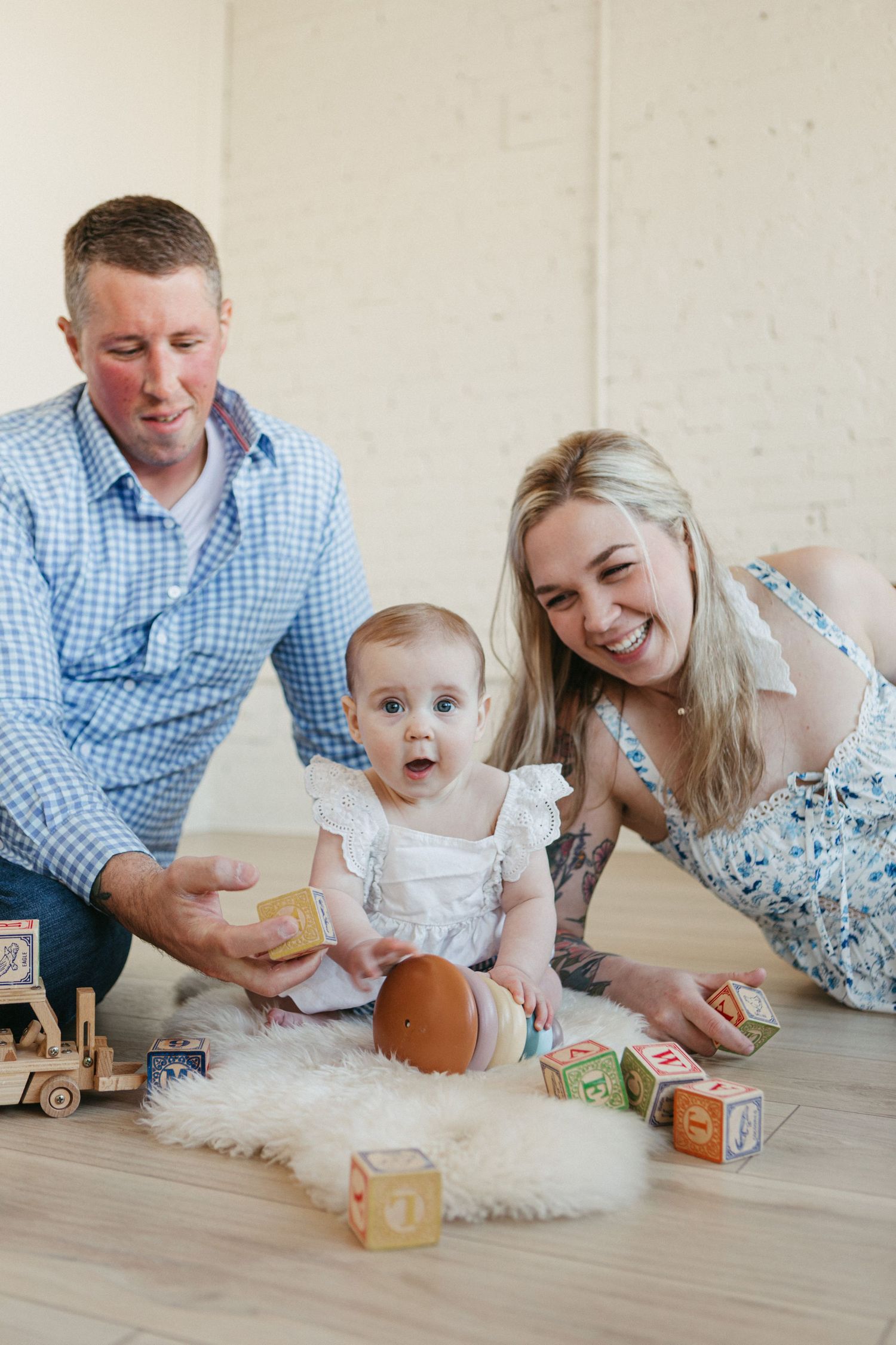 Happy family with baby playing with wooden alphabet blocks on floor, smiling parents enjoying playtime with infant.