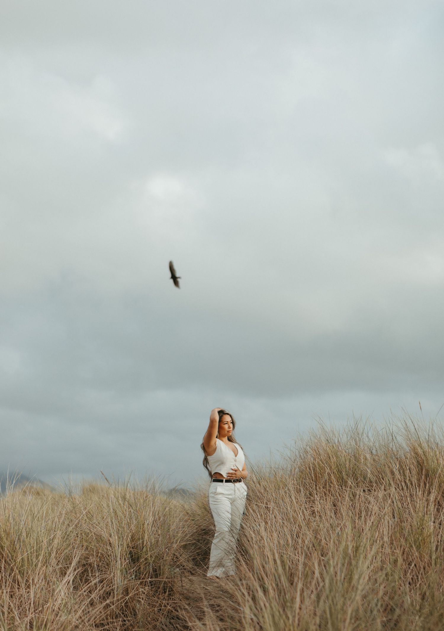 Silhouetted figures stand among tall beach grass against a moody cloudy sky at the coast.