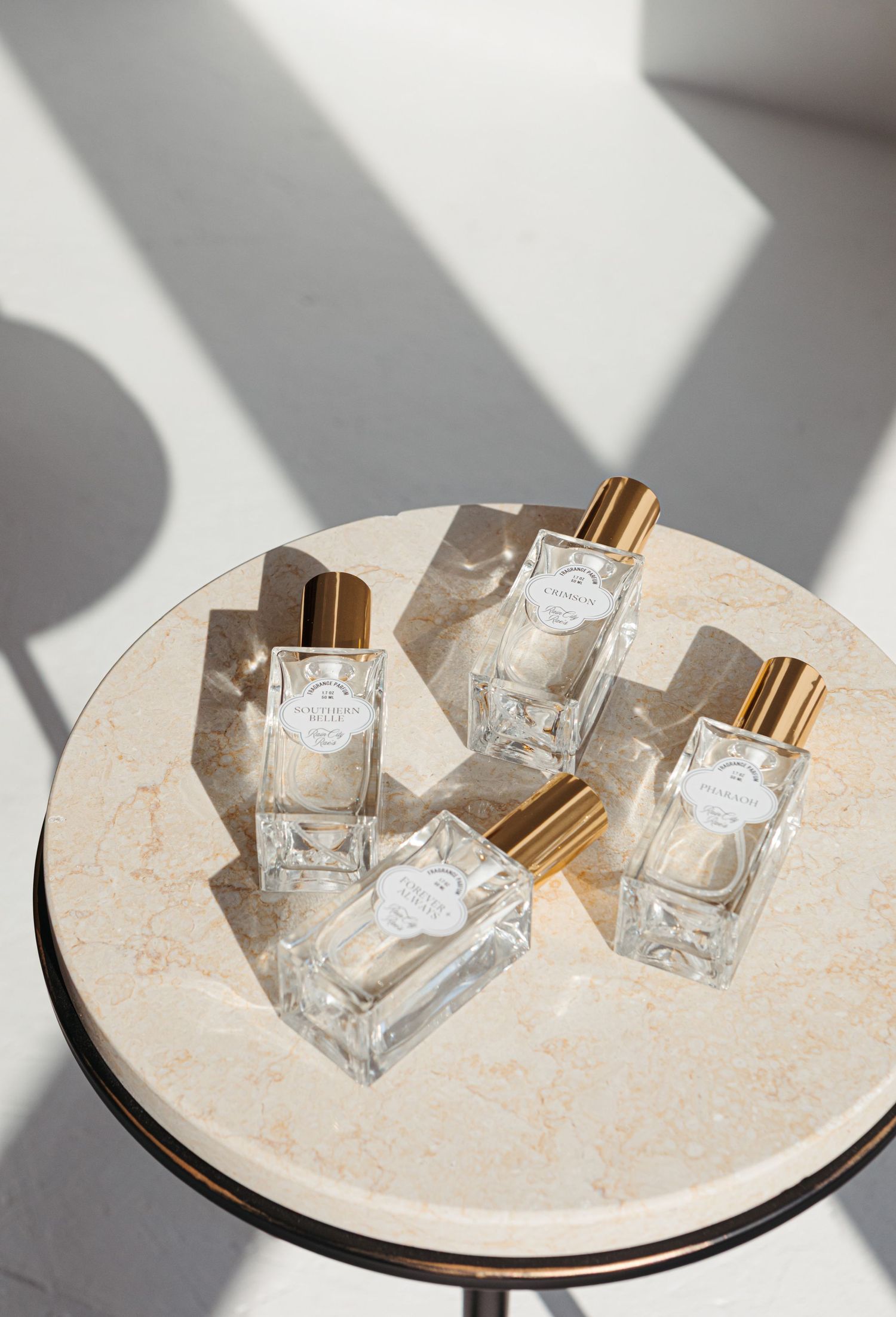 Three glass perfume bottles cast dramatic shadows on a round marble surface in natural lighting.