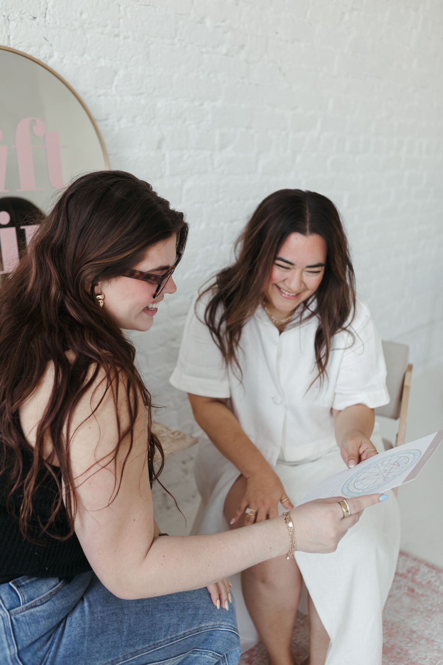 Two women sharing a lighthearted moment while looking at paperwork together in a bright white room.