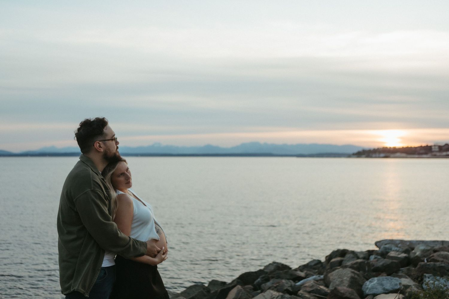 A scenic sunset view over a calm ocean with silhouettes of people on the shoreline at dusk.