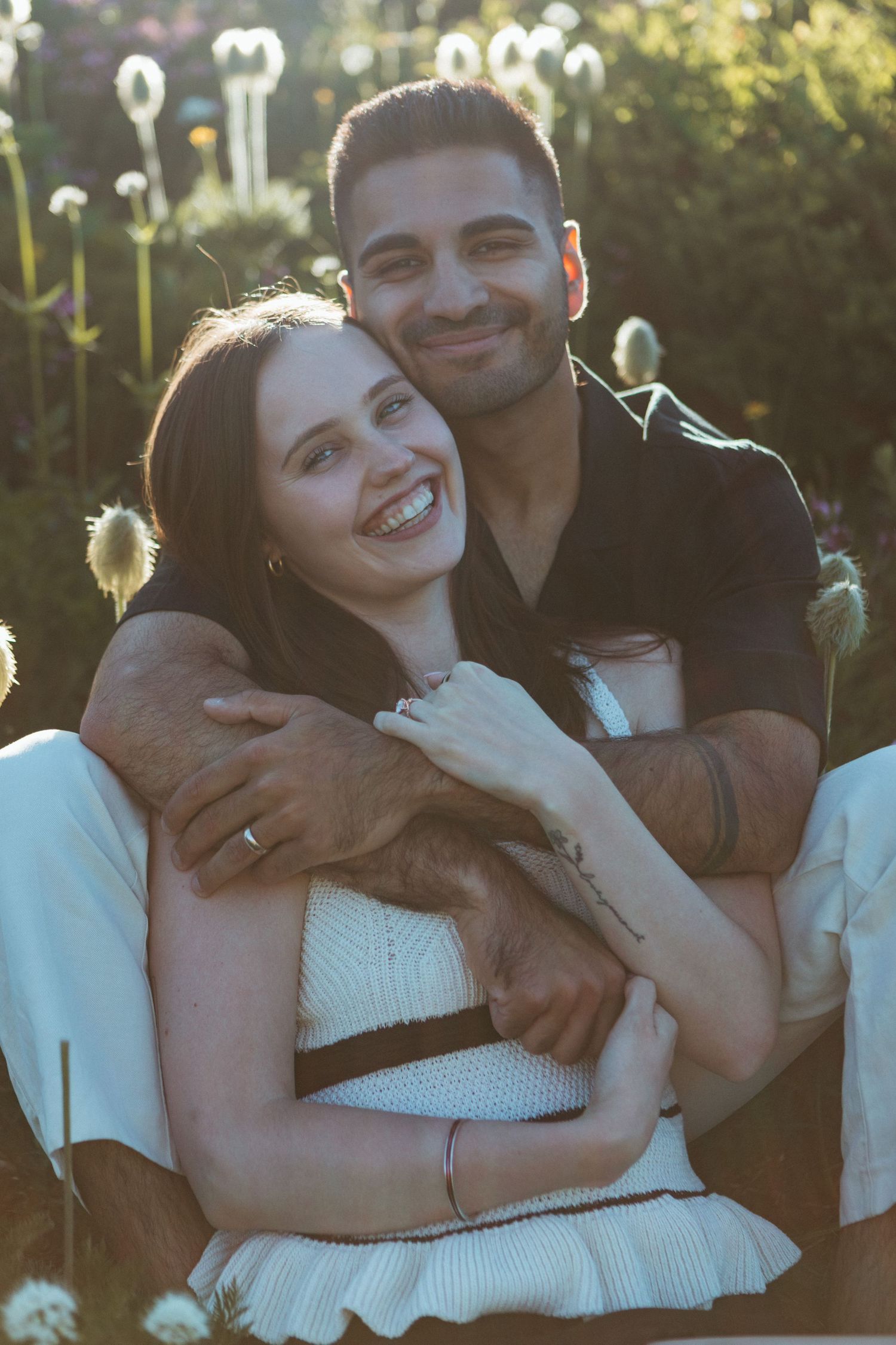 Couple shares joyful moment together in garden with backlit dandelions creating dreamy atmosphere.