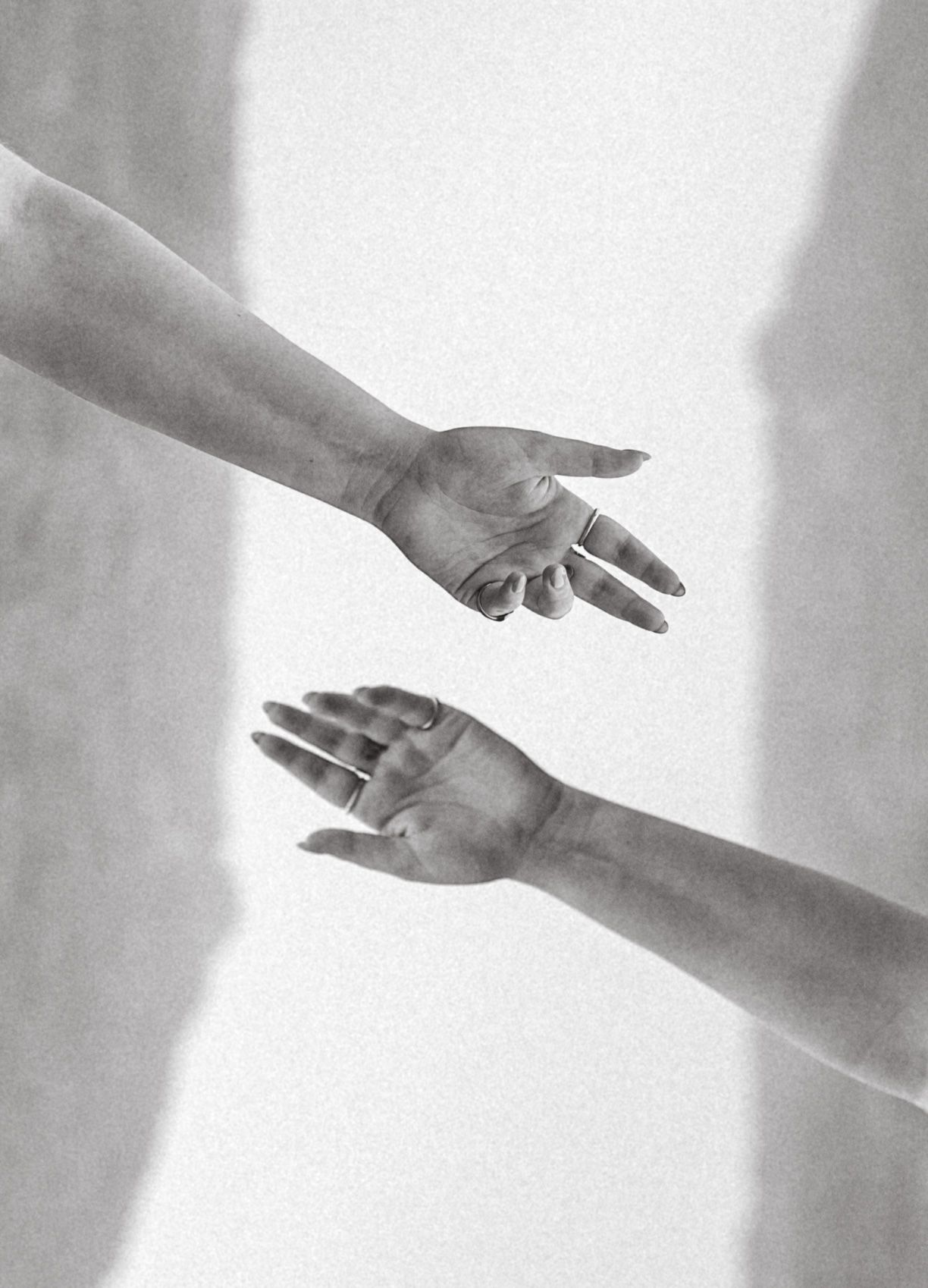 Two hands reaching towards each other in a dramatic black and white composition against a light background.