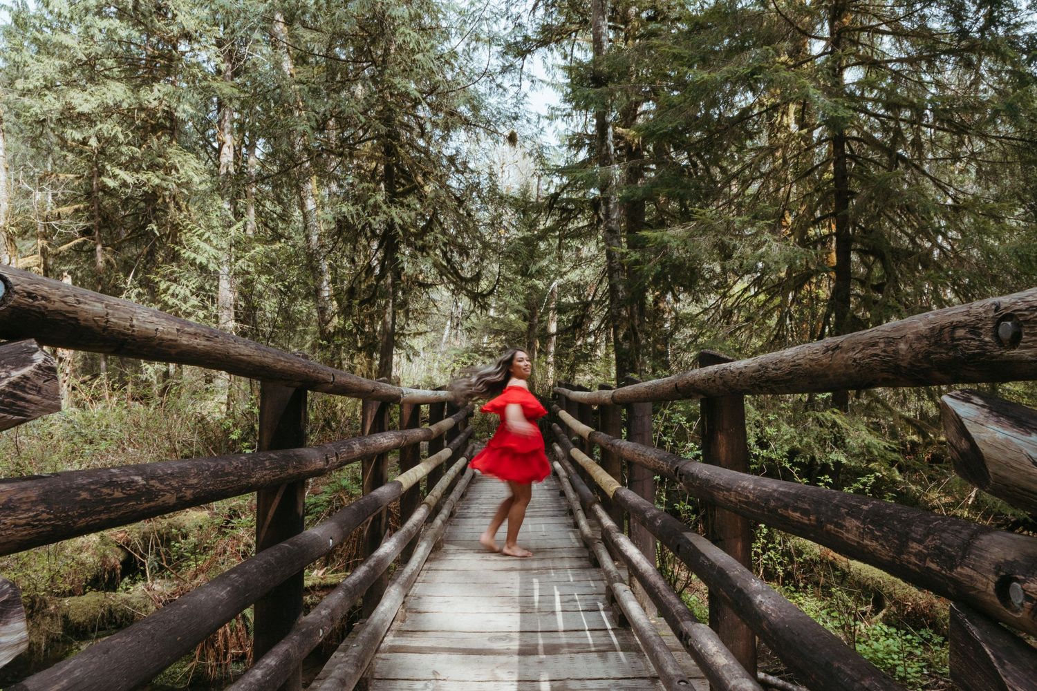 A wooden boardwalk path winds through a lush green forest with tall trees and natural lighting.